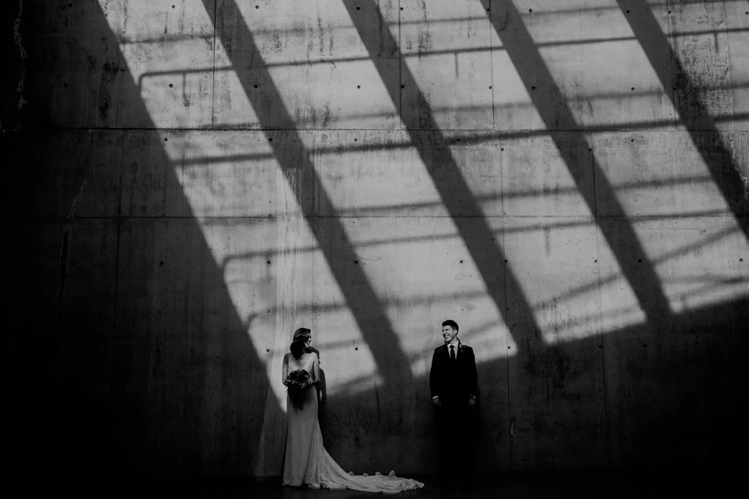 A photograph of a bride and groom standing in a mix of light and shadows in the parking garage on the campus of SAIT.