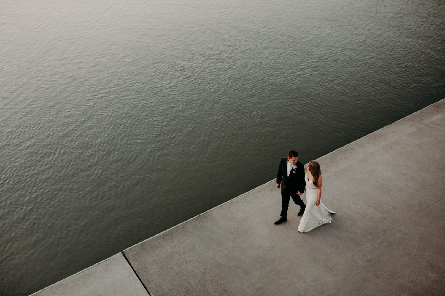 A photo taken from above as the bride and groom walk along the river at the UBC Boathouse in Richmond, BC.