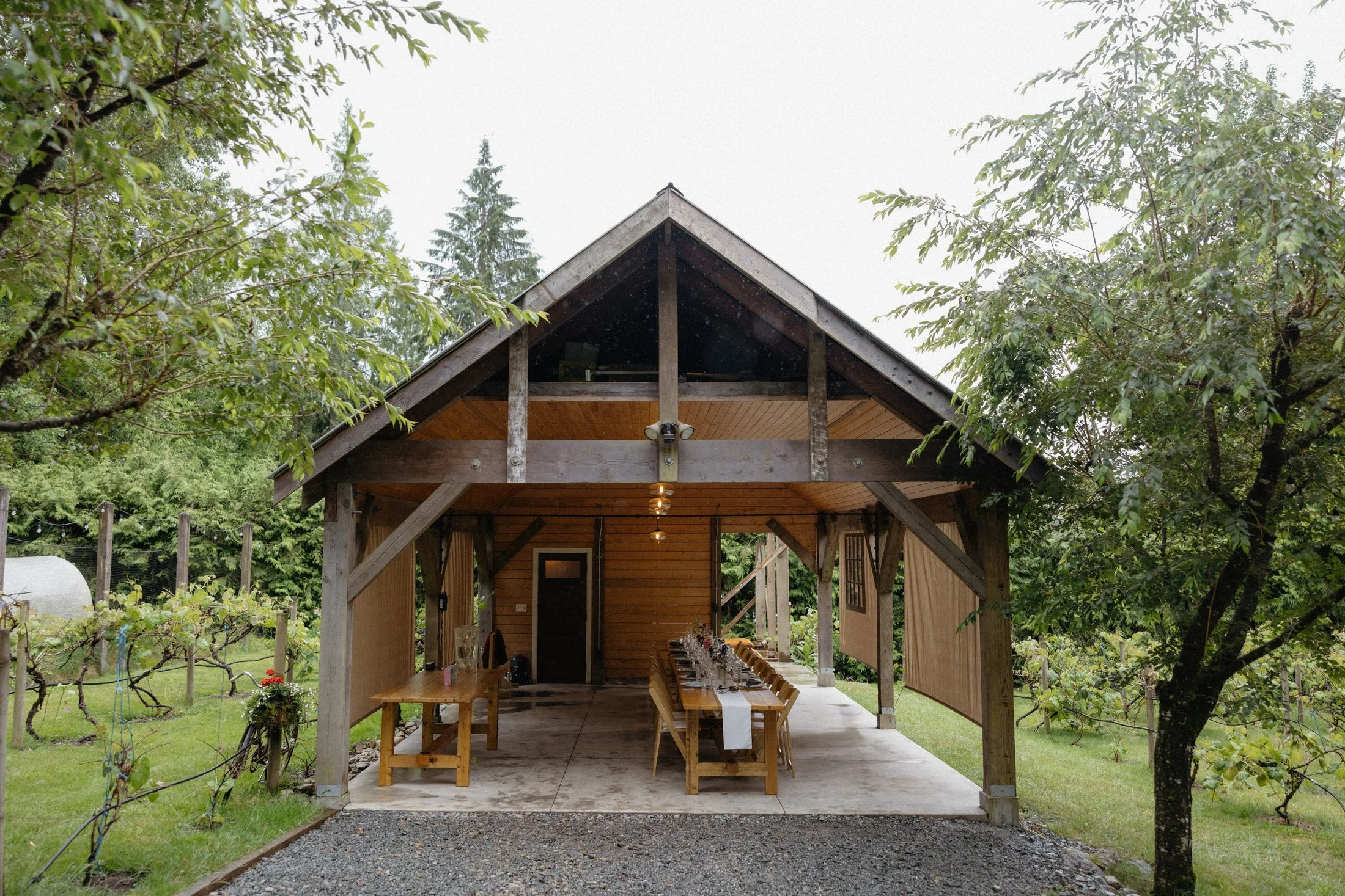 a view of the covered reception area at the greenhouse venue with a row of tables and chairs set up and a table for serving, perfect for a rainy day