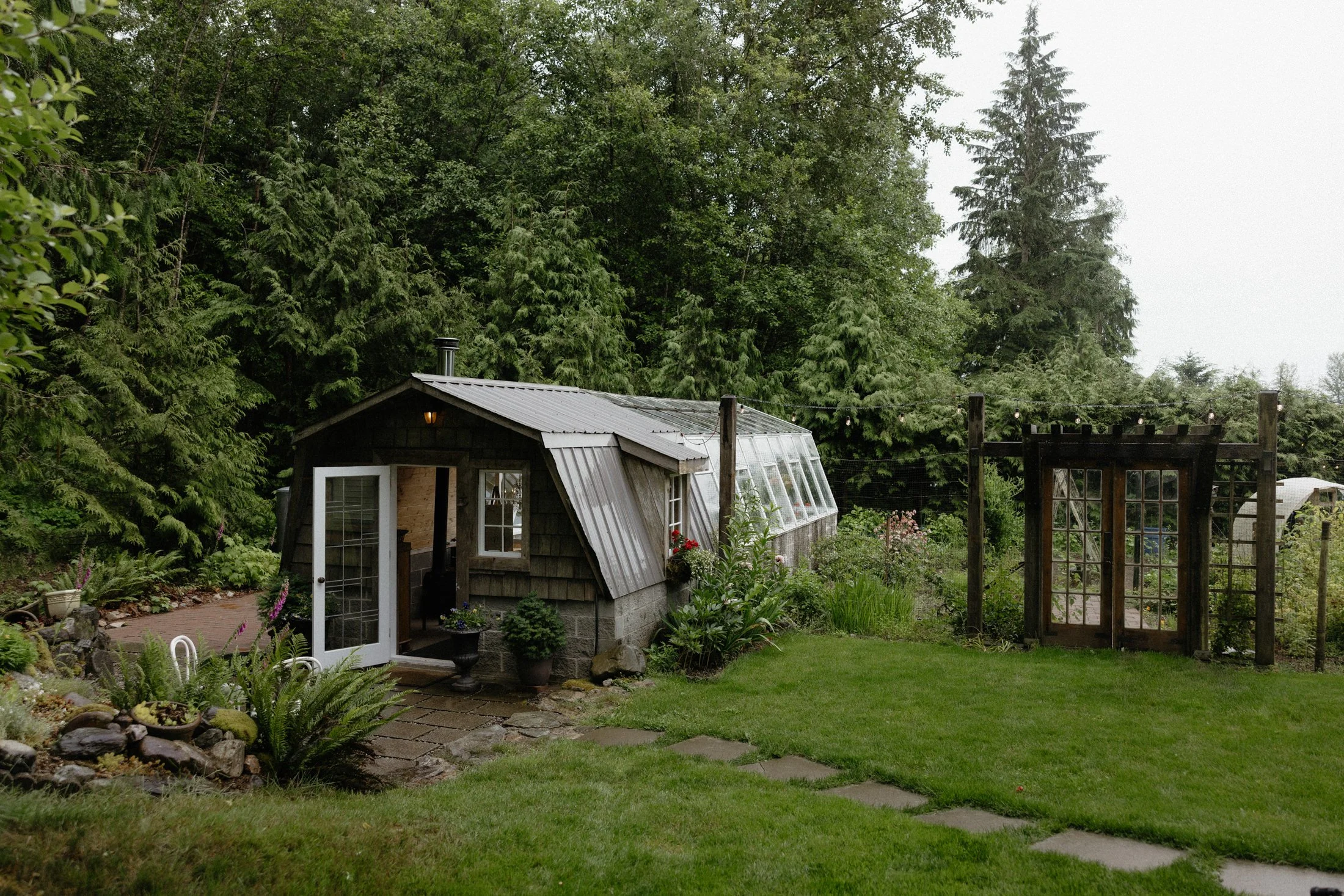 An outside view of the ceremony space at the greenhouse venue in abbotsford, complete with a wall of green trees in the background and a garden beside it