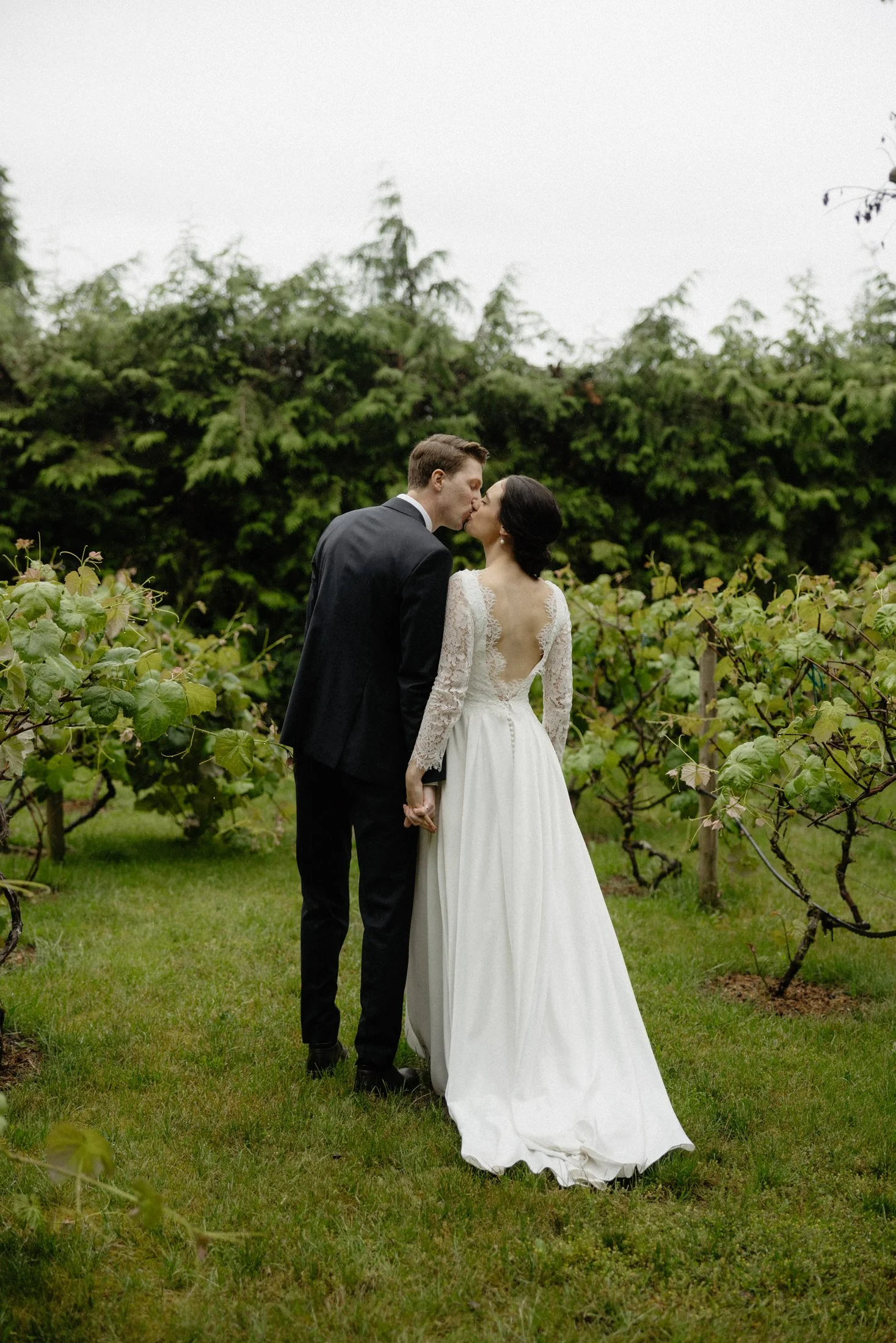 a newly married couple kissing in the vineyard part of the greenhouse venue on a cloudy day