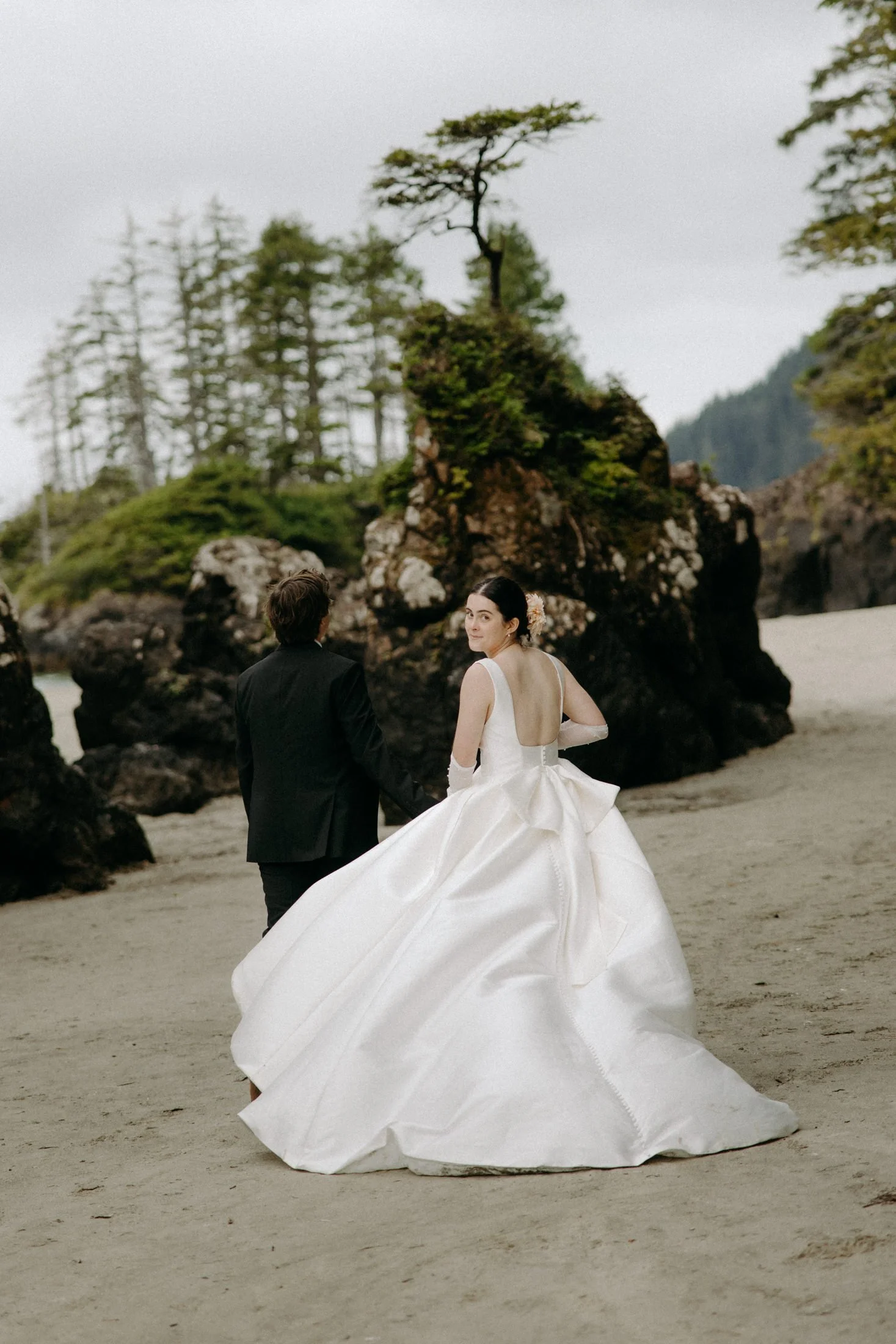 An elopement couple walks hand in hand down the beach with the sea stacks of san josef bay in the background