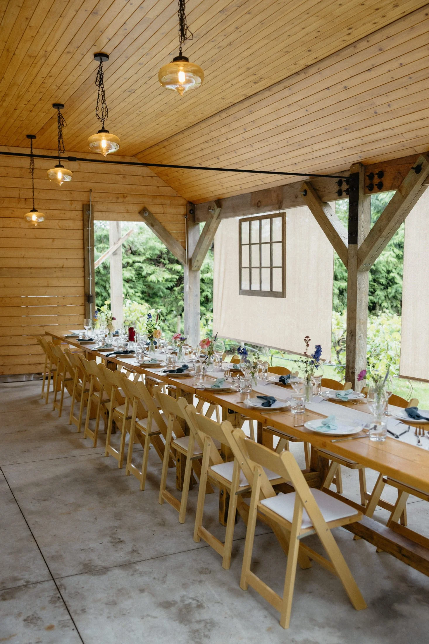 a view of the covered reception area at the greenhouse venue with a row of tables and chairs set up and a table for serving, perfect for a rainy day