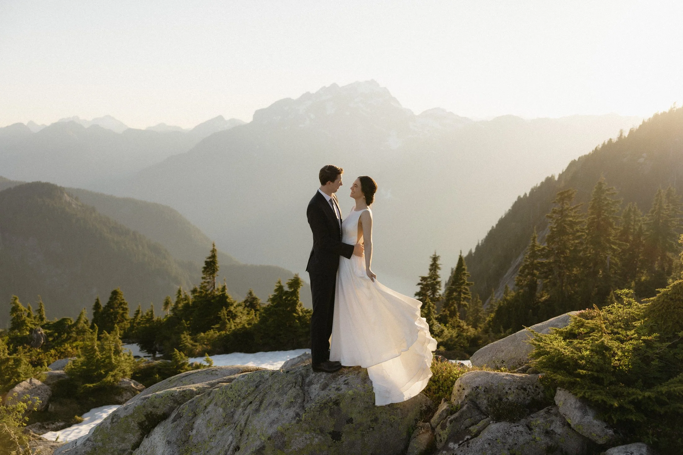 a couple embraces in the sunshine with mountains and trees in the background, made possible by bc helicopters