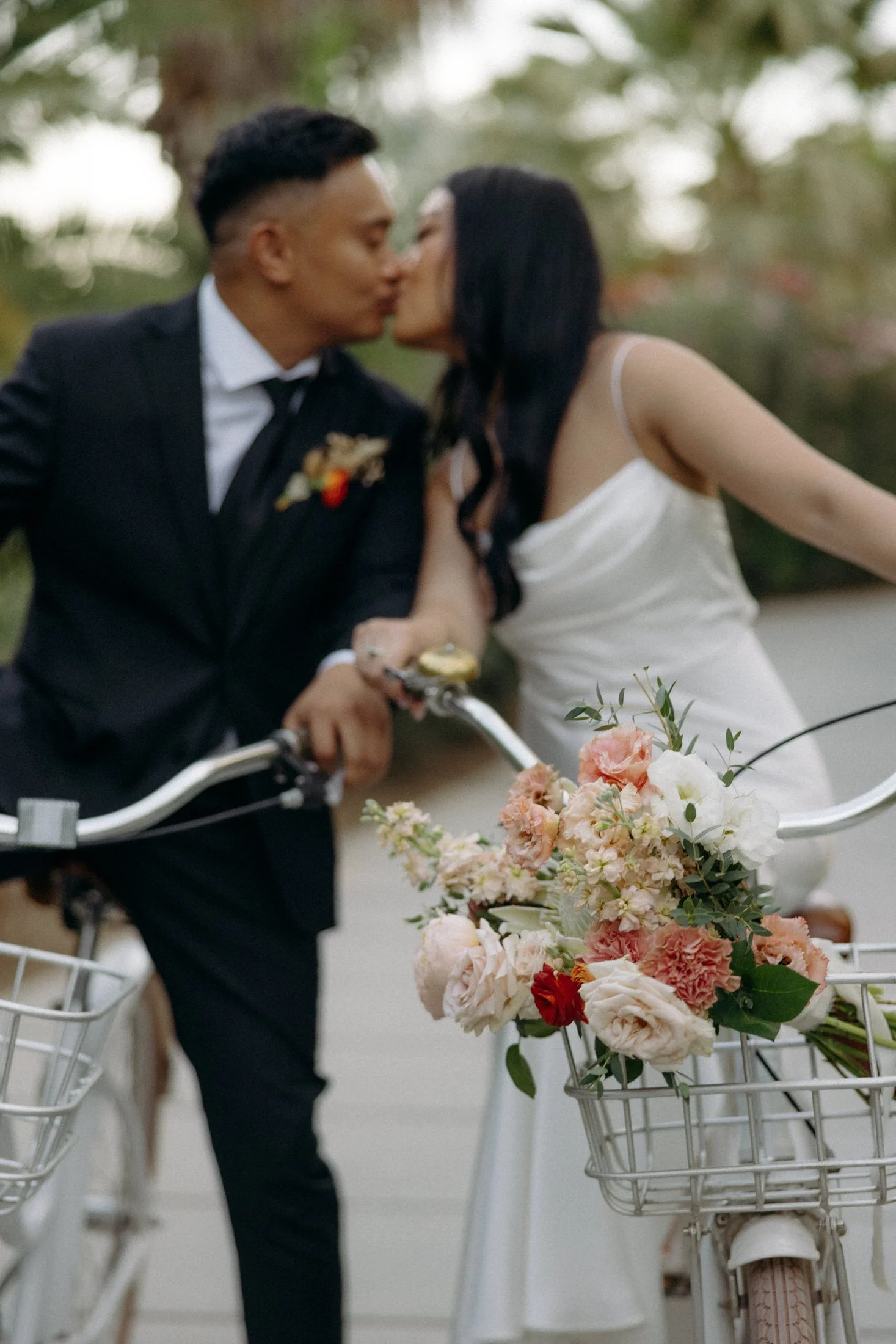 a wedding elopement couple kisses on their bikes on a path through a forest of palm trees at the acre resort in cabo, mexico