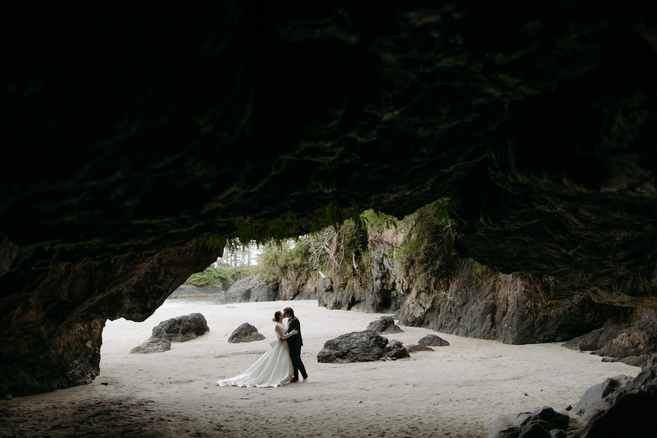 An elopement couple kissing on the beach from the view of a sea cave at san josef bay in cape scott provincial park