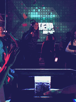 People dancing at a party, with a woman holding a gun and confetti falling around her.