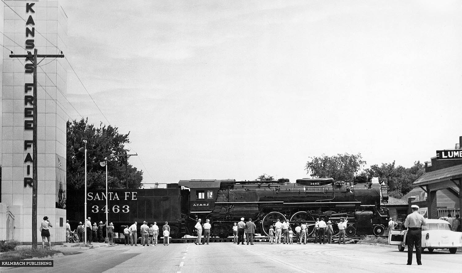 Blocking the road for only 90 minutes the ATSF shoved locomotive 3463 into the Kansas Free Fair grounds using an idler flat car (visible in front of the steam engine) and a diesel-electric switch engine. Image courtesy of Kalmbach Publishing Co.