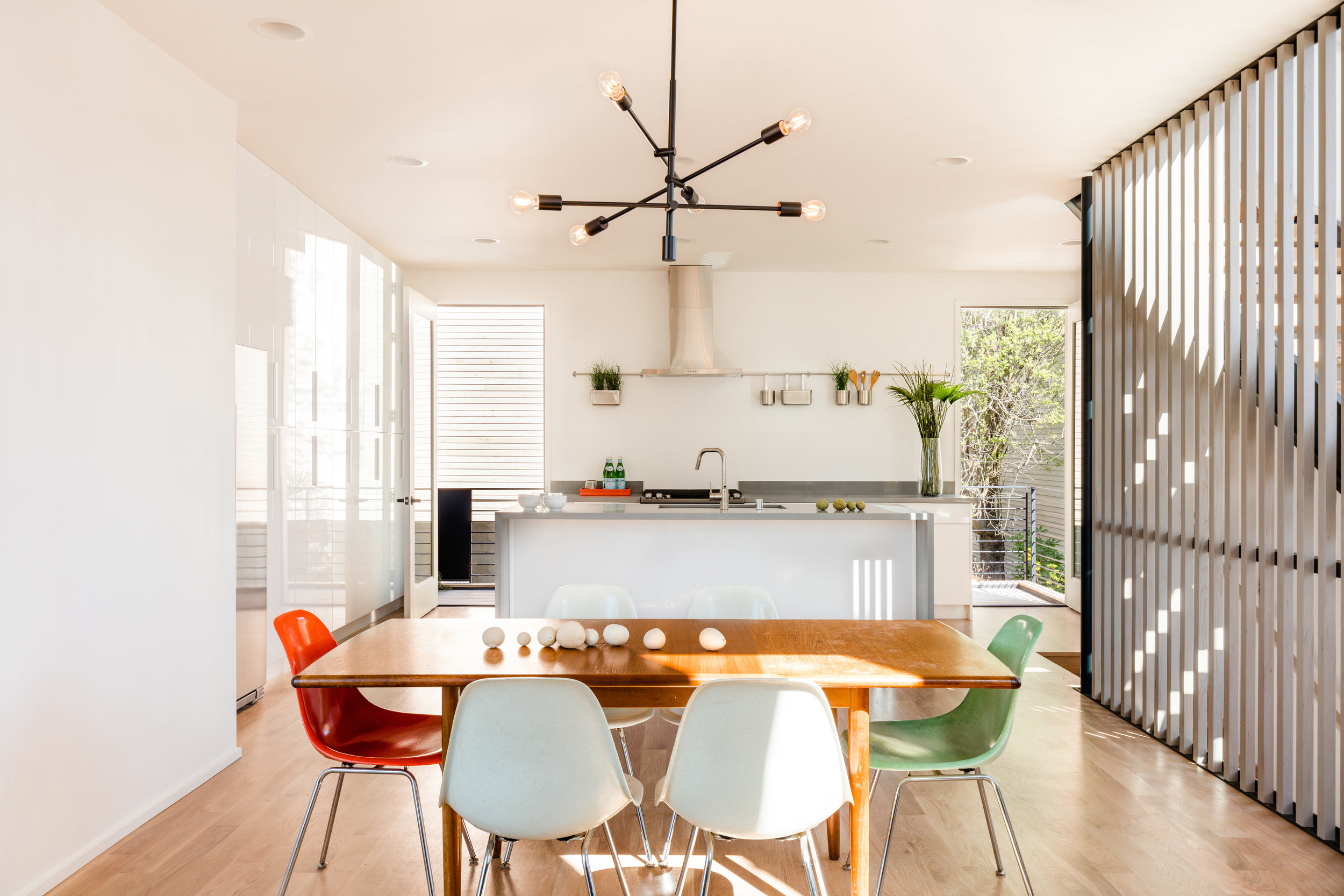 The main house living area is open to the dining and kitchen, with large doors opening to an outdoor deck to the east. The high gloss casework reflects the outdoor light and textures and brings nature into the interiors.