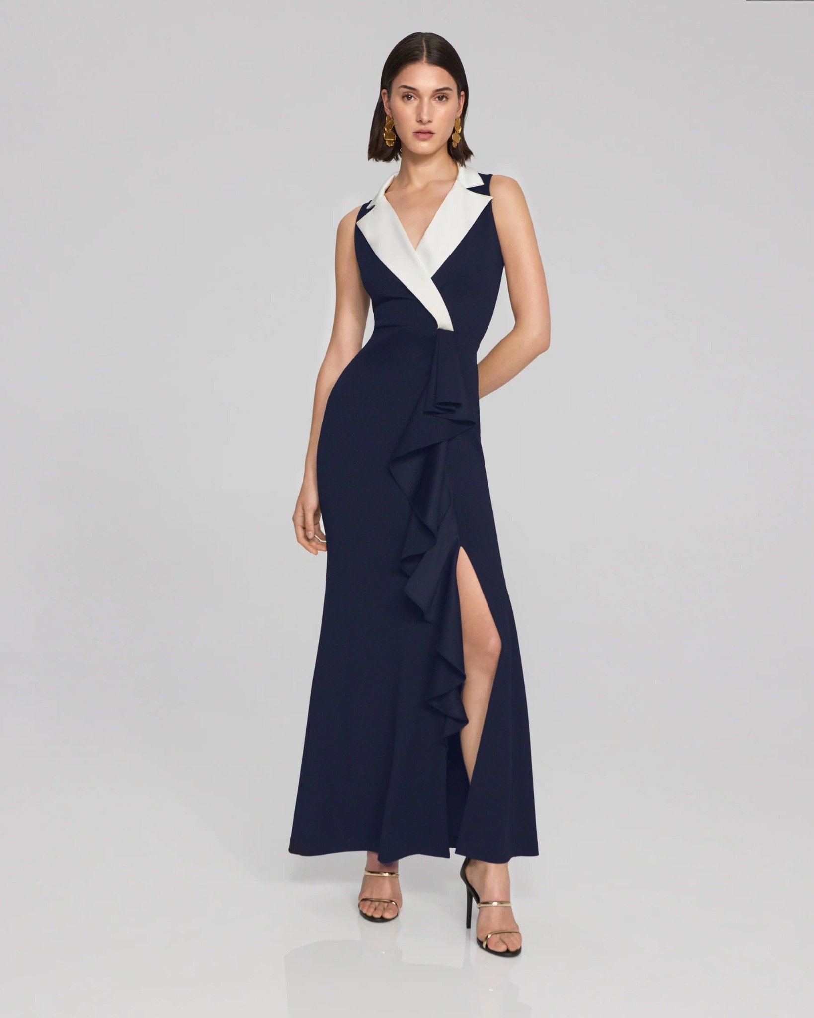 Step into the spotlight with this solid scuba crepe tuxedo-style gown. This stunning trumpet maxi dress features a notched collar in a contrasting colour for a touch of contemporary flair. The front ruffle and left-side slit add a playful yet elegant