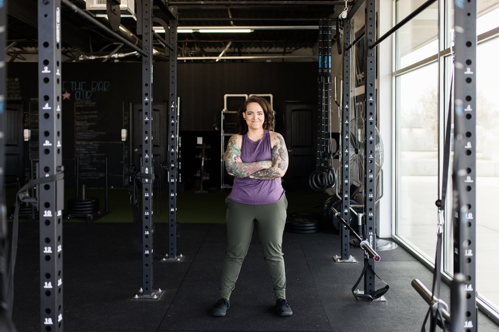 okc oklahoma norman commercial photography woman with backwards hat and brown hair with tattoos standing cross armed in the gym with smirk headshots branding photography