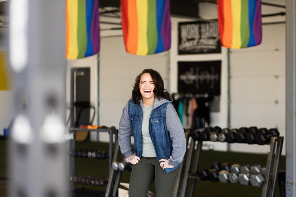 okc oklahoma norman commercial photography woman with brown hair with tattoos under pride flags laughing in the gym headshots branding photography