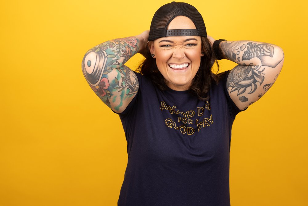 okc oklahoma norman commercial photography woman with backwards hat and brown hair with tattoos on yellow background headshots branding photography