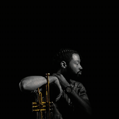 A man holding a trumpet in a dark setting, looking to the side.