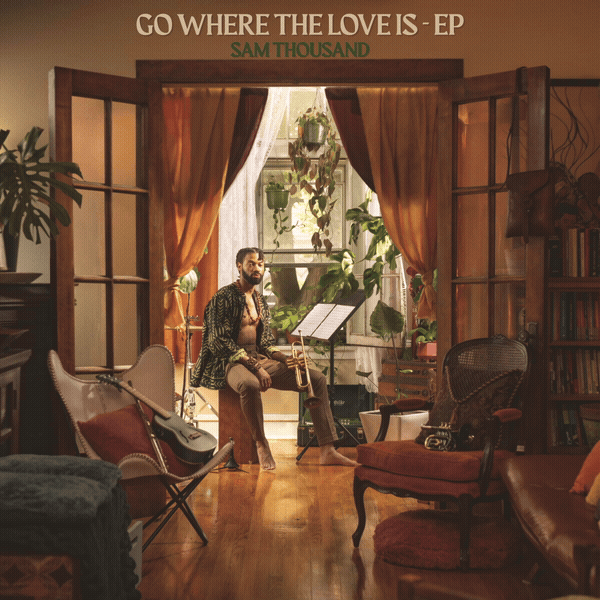 A man is sitting with a trumpet in a cozy, vintage-style living room, surrounded by plants, bookshelves, and musical instruments, with open wooden doors leading to a balcony filled with greenery.