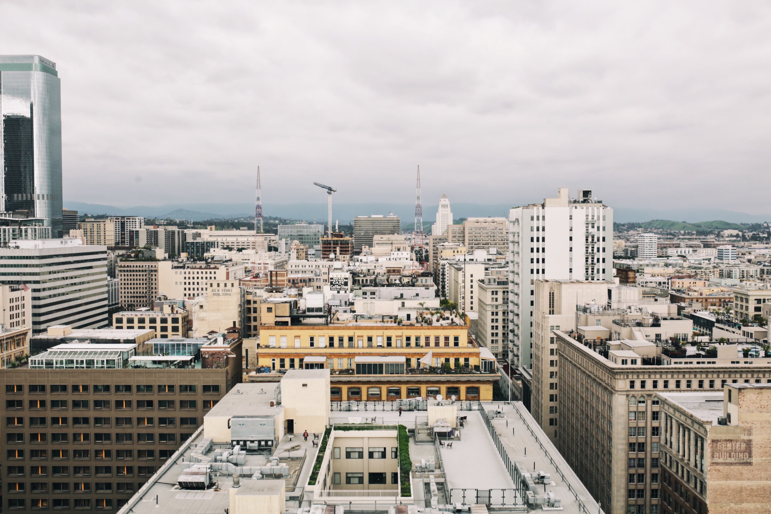 City skyline with tall buildings, some cranes, and cloudy sky.