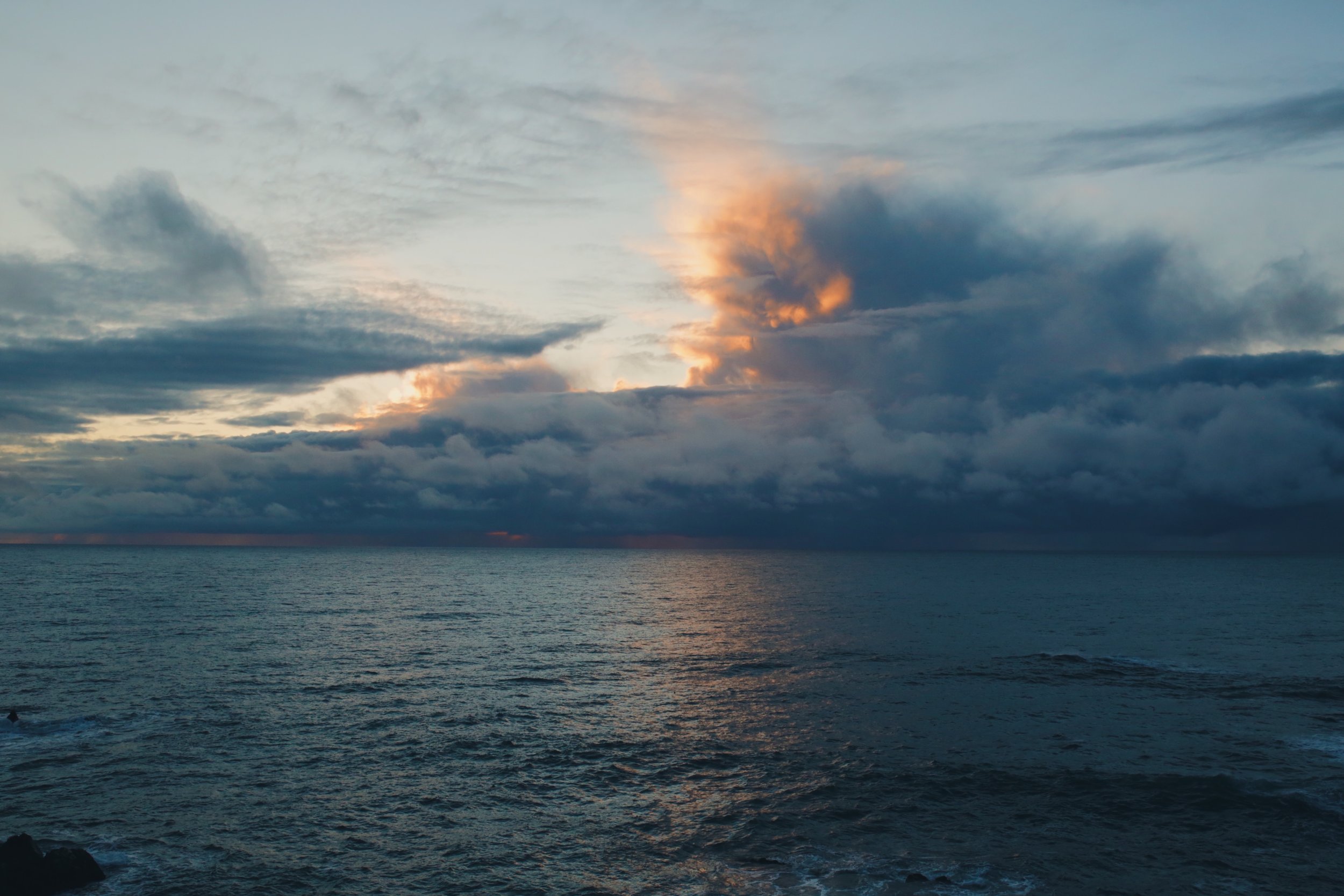 A serene ocean view during sunset with dark clouds and colorful sky.