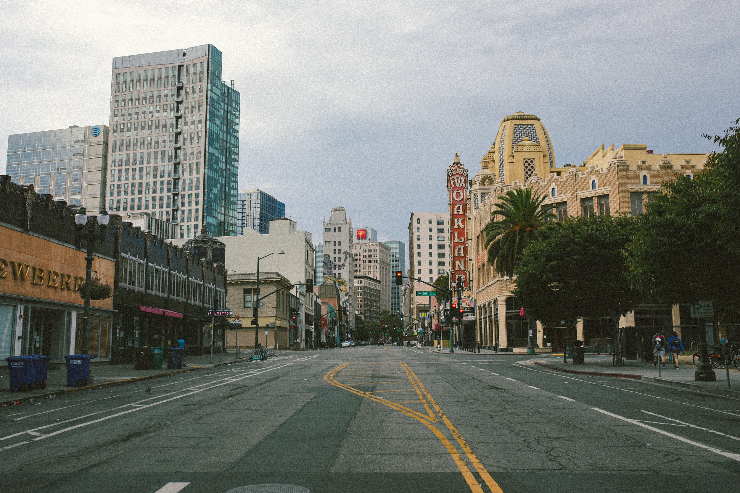 Empty city street with tall buildings, palm trees, and a historic-looking building with a marquee reading 'Fox Oakland' in downtown Oakland, California.