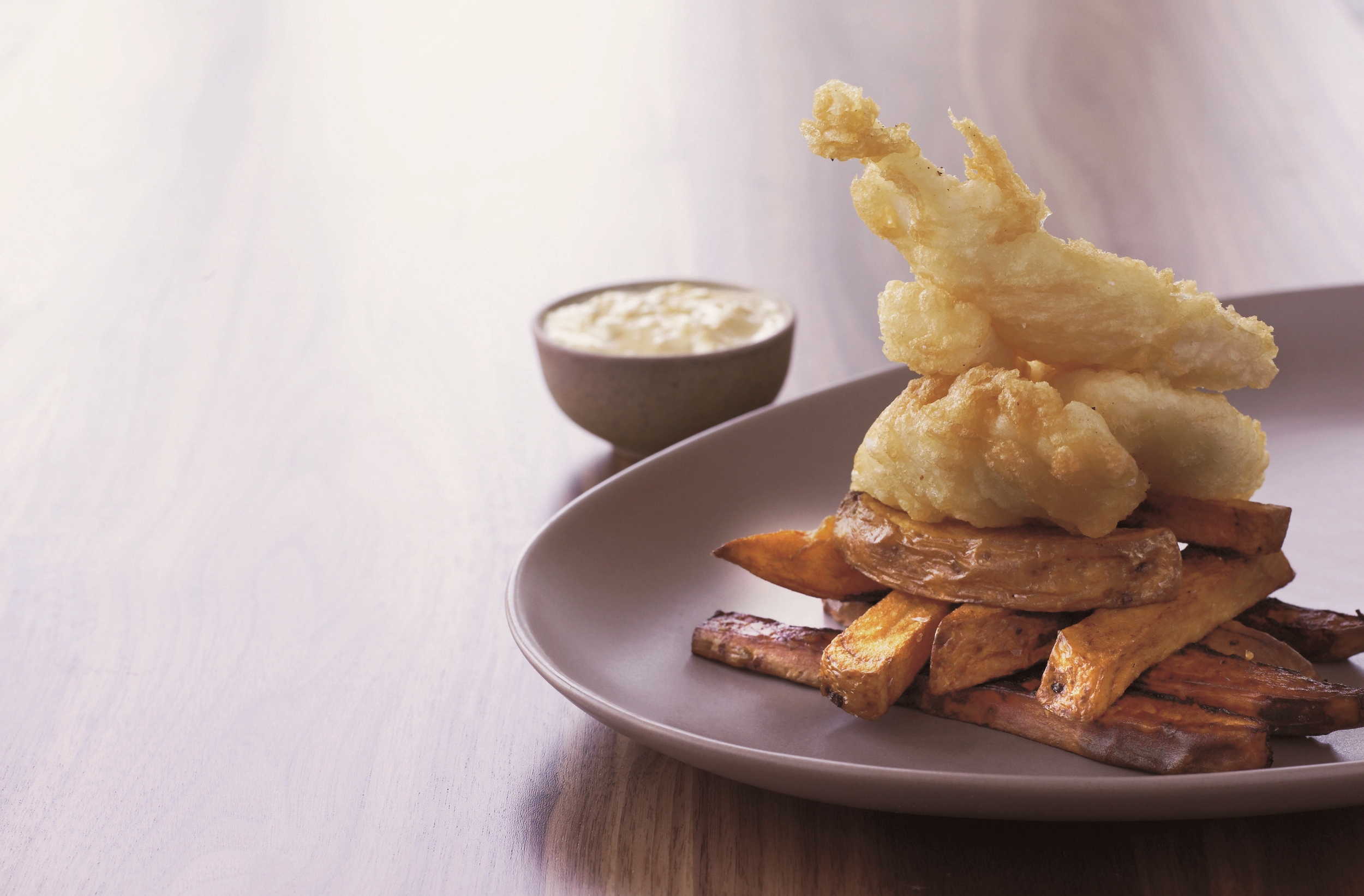 Photo by Lars Ranek Japanese Fish & Chips Served w/ Danish Remoulade This recipe dates back to 2002 and became one of the most popular dishes on the menu for the sushi chain I just to take care of. Originally served with chips made of half and half of potato and sweet potato. This was in many ways most ambitious fusion for years - Japan meets Britain with a Danish detour. The Danish influence is the tradition of serving fish and chips with remoulade sauce (something totally forbidden in my childhood) which is a wonderful medley of homemade mayonnaise and piccalilli style pickles, packed with turmeric, not only adding a beautiful color, but also brilliant for it anti-inflammatory qualities. The quantity of pickled vegetables in this recipe is much more than you will need for one batch of remoulade sauce, but it's the sort of thing that is impractical to make in smaller amounts. Keep the pickles in a sterilized jar in the fridge for up to 3 months, suing them for meat, cheese or even more luscious remoulade. For fish the best choice fish I would recommend cod, hake, haddock or coley, all 4 species are now MSC certified and therefor the best ethical option. Serves 4 1 fillet of white fish, about 600-700 grams, skinned 2 large sweet potatoes 2 large white potatoes, like Maris Piper or Edwards 3 liter sunflower oil for frying For the pickles 2 large carrots Small head of cauliflower Small head of broccoli 4 sticks celery 1 small butternut squash 300 gram caster sugar 1 tablespoon mild curry powder 1 tablespoon turmeric 1 tablespoon whole peppercorn 4 bay leaf 1.5-2 liter of rice vinegar 3-4 tablespoon cornflour For the remoulade sauce 1 whole egg 1 egg yolk 1 tablespoon yuzu juice 1 tablespoon rice vinegar 1 tablespoon sugar 50 ml, olive oil 100 ml. rapeseed oil 50 ml. sweet chili 200 ml. pickles For the tempura batter 1 egg 1 teaspoon carbonated soda 1/2 liter ice cold water 400 gram sifted OO flour Extra flour for dusting To make the pickles: peel and cut all the vegetable in 1 centimeter dices. Place vegetables in a large heavy-based saucepan with the sugar and species. Add enough rice vinegar to just cover all the vegetables completely. Bring to the boil and cook until the vegetable is al dente, aka still crunchy with a bite. Place a large colander on top of a large bowl and drain the vegetables, saving the liquid. Return all the liquid to the saucepan and bring it back to the boil. Dissolve the cornflour in a little cold water and gradually add it to the vinegar mixture to give a thick, smooth consistency (you may not need all the cornflour). Pour the sauce over the pickled vegetables, stir and set aside to cool. To make the remoulade sauce: place the egg, egg yolk, yuzu juice, rice vinegar and caster sugar in a food processor.and blend until white and fluffy. Combine the two oils and add them to the mixture gradually, blending to give an even consistency. Now poor in the sweet chili and pulse until incorporated. Decant sauce into a bowl. Place 200 ml. pickles in the food processor and pulse until coarsely mixed. Add pickles to mayonnaise and mix until all incorporated. Prepare the tempura batter: whisk the egg, add the carbonated soda, then the ice cold water and gradually ad the flour until the mixture is lumpy and airy with a consistency similar to double cream. Place in the fridge to chill. Place the cod (or other white fish) on a chopping boar and cut down the middle following the line in the middle of the fillet. Trim of any flabby bits and discard. Cut the fillet diagonally into 1 centimeter thick slices, working at a 45-degree angle so that each piece is cut on the bias. Aim for 12 equal sized pieces. Cut both varieties of potatoes into chips. Keeping the batches separate, rinse them in cold water and leave to rest in a colander. Heat the oil to 180 degrees Celsius in a deep fat fryer or large heavy-based saucepan. When the oil is ready fry each batch of potatoes for 4 minutes, leaving to rest in grease proof paper lines tray. Leave to cool down. Dust the cod pieces in flour, then dip them in the chilled tempura batter 4 pieces at the time. Fry for approximately 3 minutes until light golden and crisp, then drain on grease proof paper and season with sea salt. Repeat with the remaining fish. Finally re-fry potatoes for 4 minutes, drain and season with sea salt. Stack chips, place cod on to and serve with remoulade in a small pot on the side. 