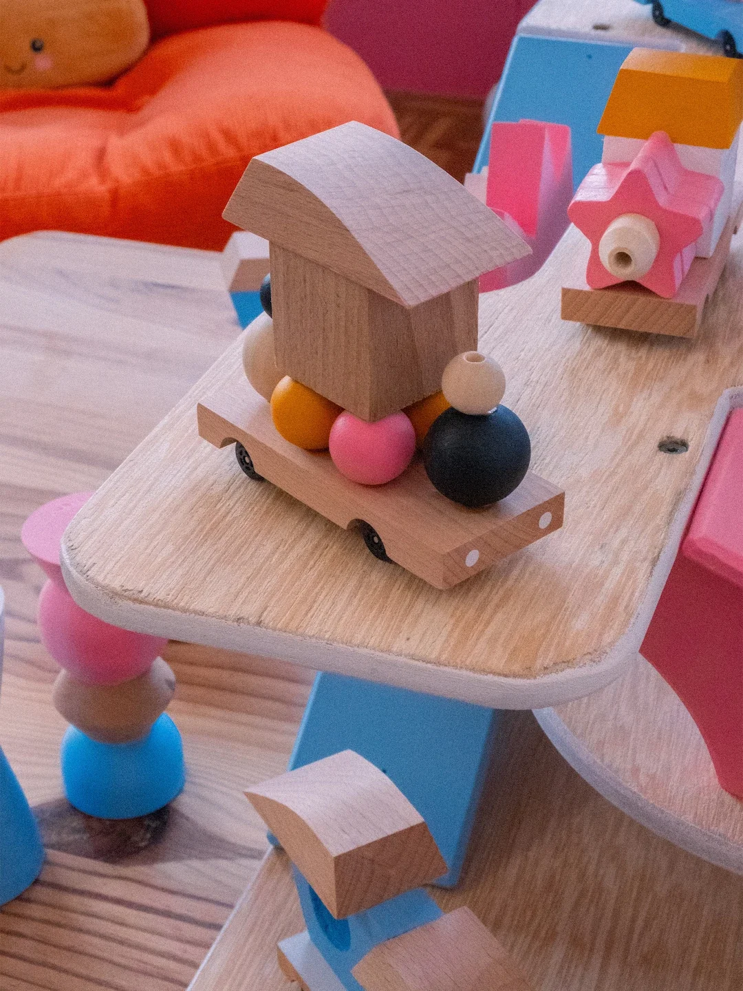 Jeu de construction en bois avec des pièces colorées et naturelles, y compris un véhicule avec un toit en bois et des boules en bois de différentes couleurs, sur une table en bois.