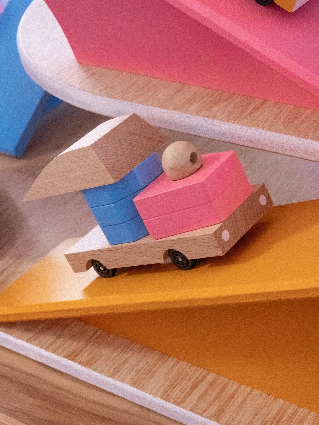 Un jouet en bois représentant une petite remorque avec des blocs de bois colorés, un bois rond et des roues en plastique.