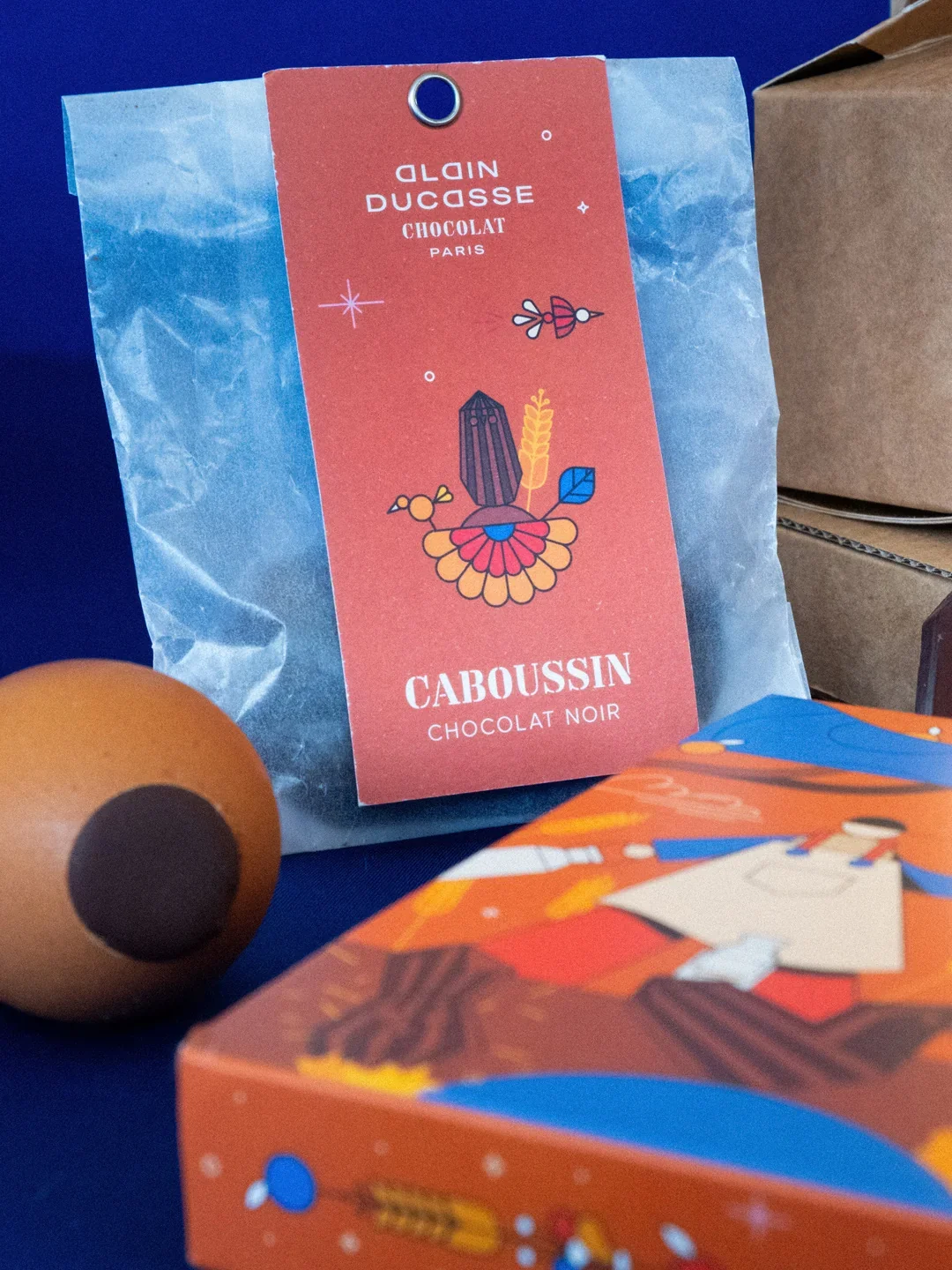 Paquet de chocolat noir de la marque Caboussin avec un design coloré, en arrière-plan un jouet en bois. 