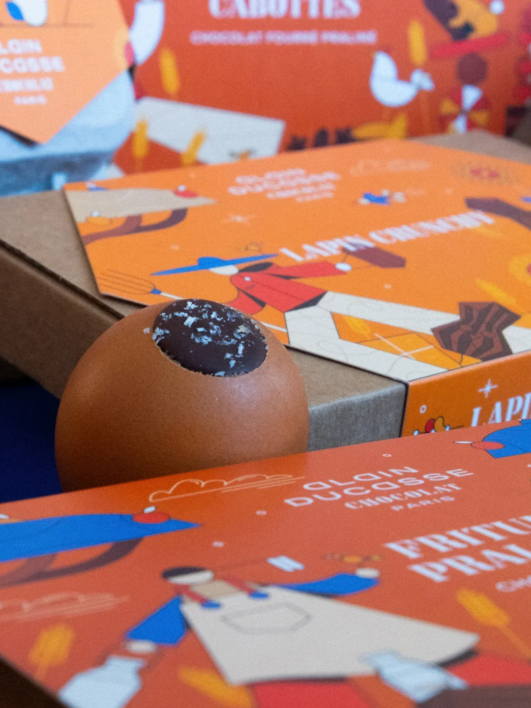 Oeuf en coquille brisé avec du chocolat noir à l'intérieur, entouré de boîtes orange décoratives à thème de Noël.