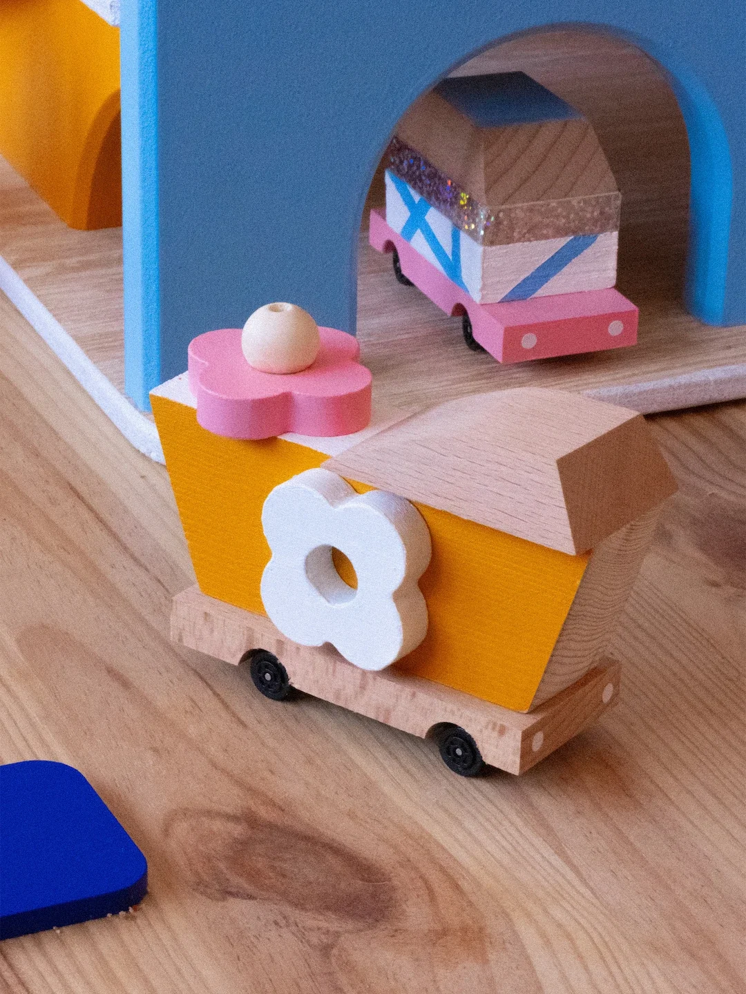Un jouet en bois représente un train coloré avec des détails en rose, blanc, bleu et beige, placé sur une surface en bois.