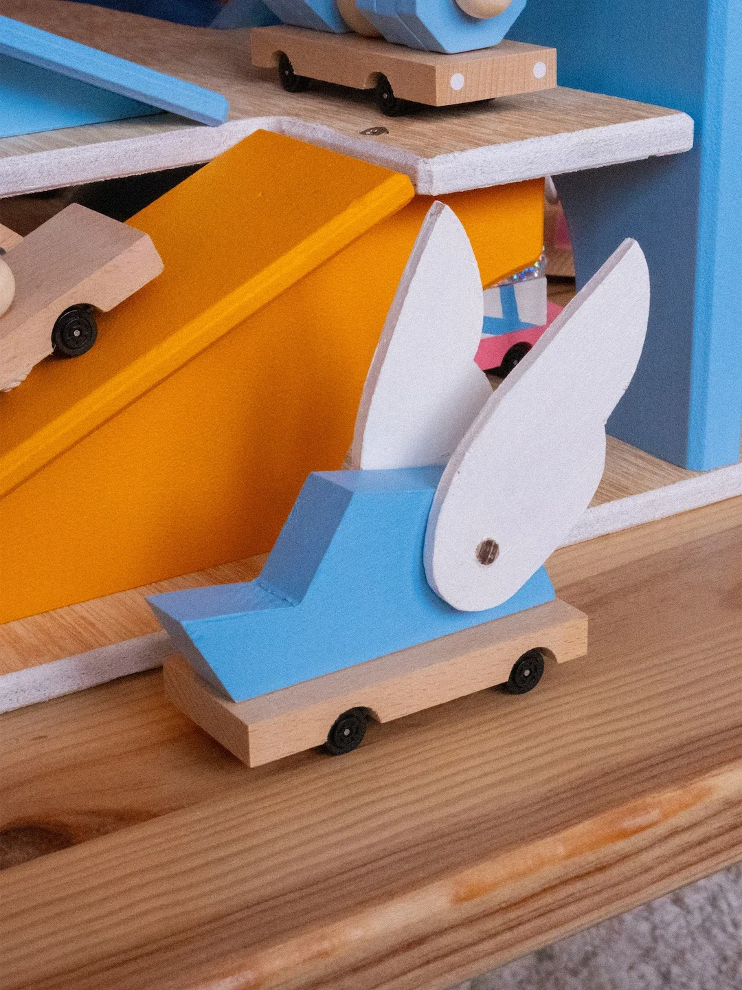 Un jouet en bois représentant un lapin bleu avec de grandes oreilles blanches, placé sur une petite plateforme à roulettes.