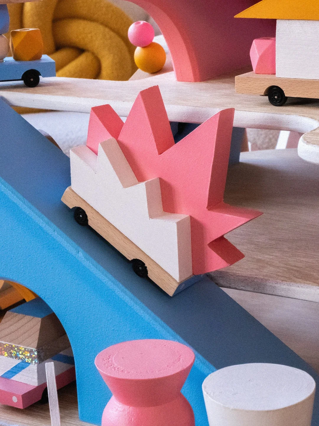 Une structure en bois peinte en pastel avec des formes géométriques, des arches, des roues et des éléments en forme de montagnes et de cercles, conçue comme un parcours de jeux ou un jouet pour enfants.