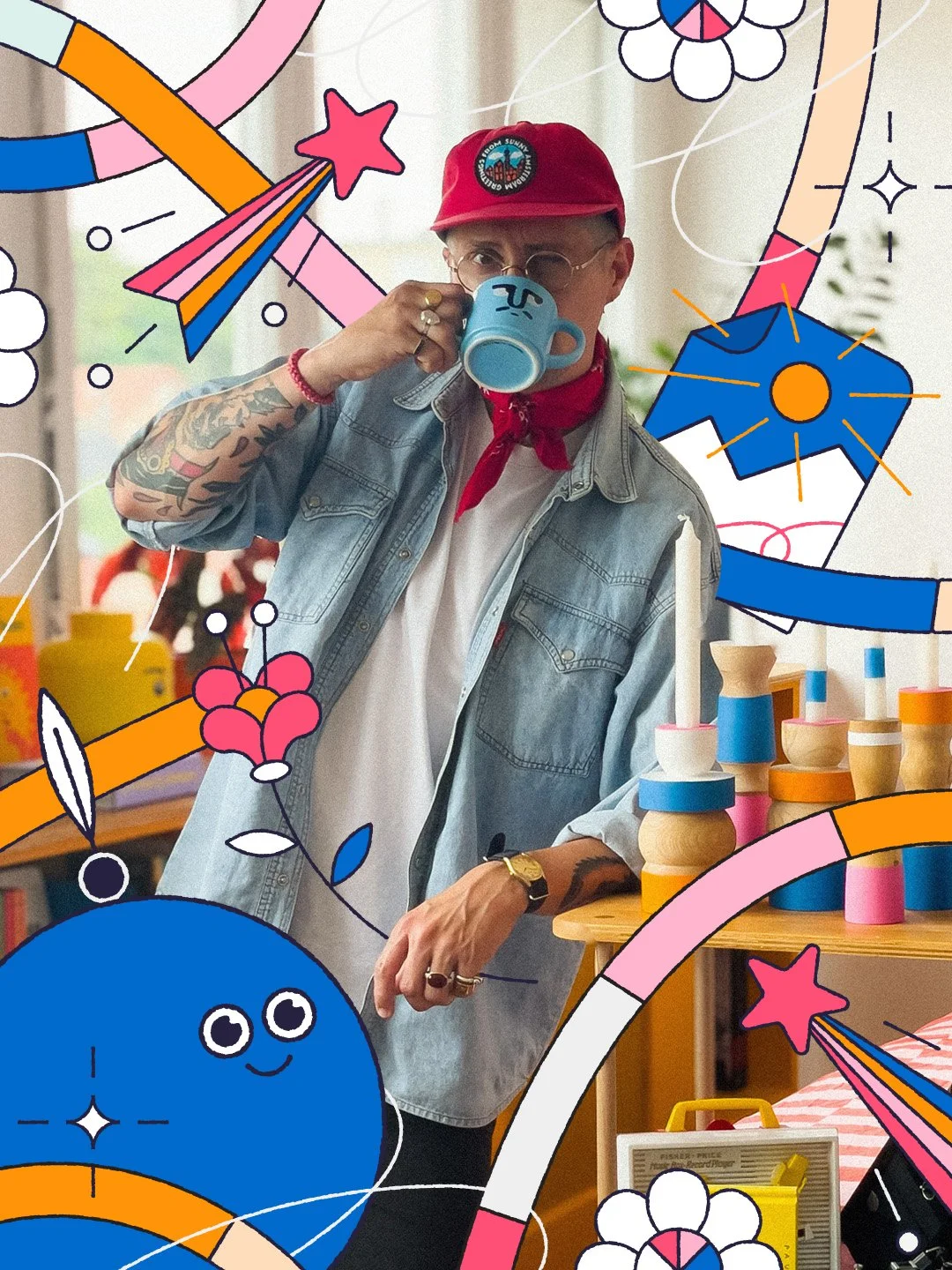 Une personne portant un chapeau rouge, des lunettes rondes, une chemise en denim, et buvant dans une tasse bleu avec un visage dessiné, entourée de décorations colorées et de jouets en bois sur une table.