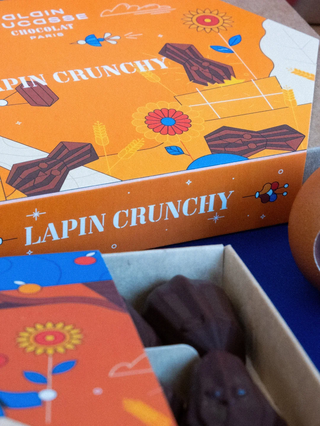 Boîte d'emballage de biscuits au chocolat "Lapin Crunchy" avec illustration de lapins, fleurs et blé sur un fond orange