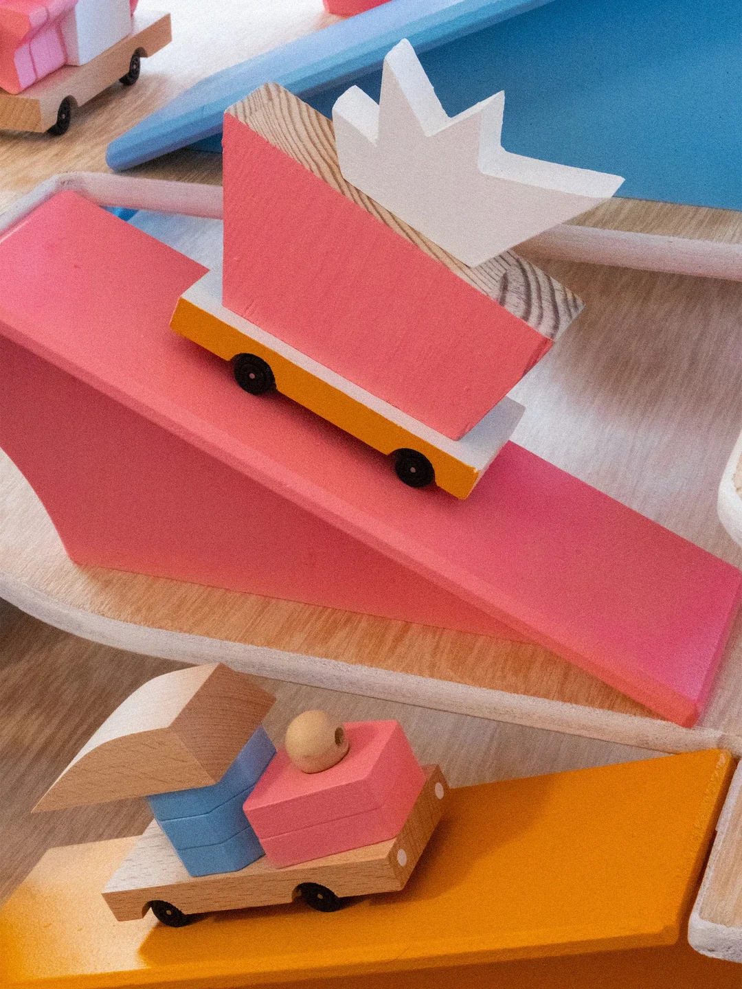 Deux jouets en bois colorés imitant des voitures, avec des moulins à vent et des éléments décoratifs, disposés sur une surface en bois.