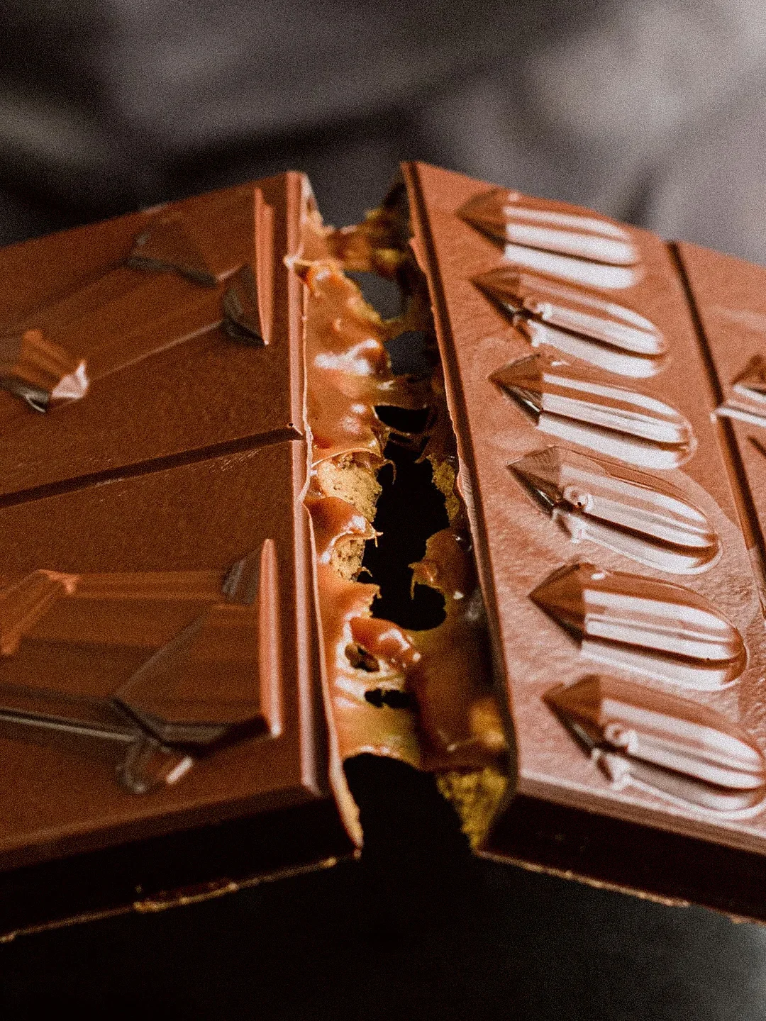 Une boîte de chocolats avec plusieurs pièces intactes et une pièce cassée, révélant un intérieur de caramel, de biscuits et de chocolat.