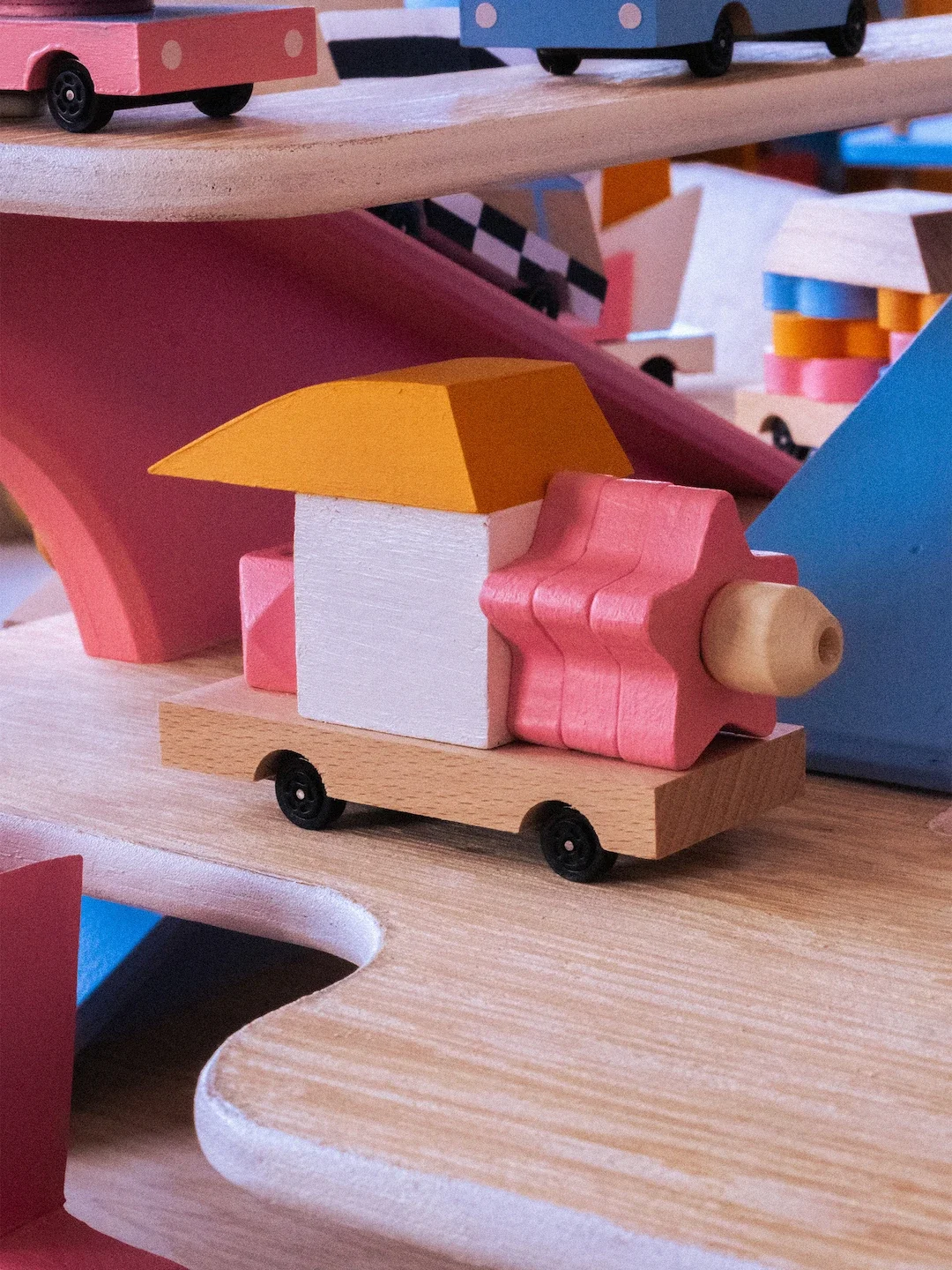 Voiture en bois colorée avec des formes géométriques, installée sur une rampe de bois.