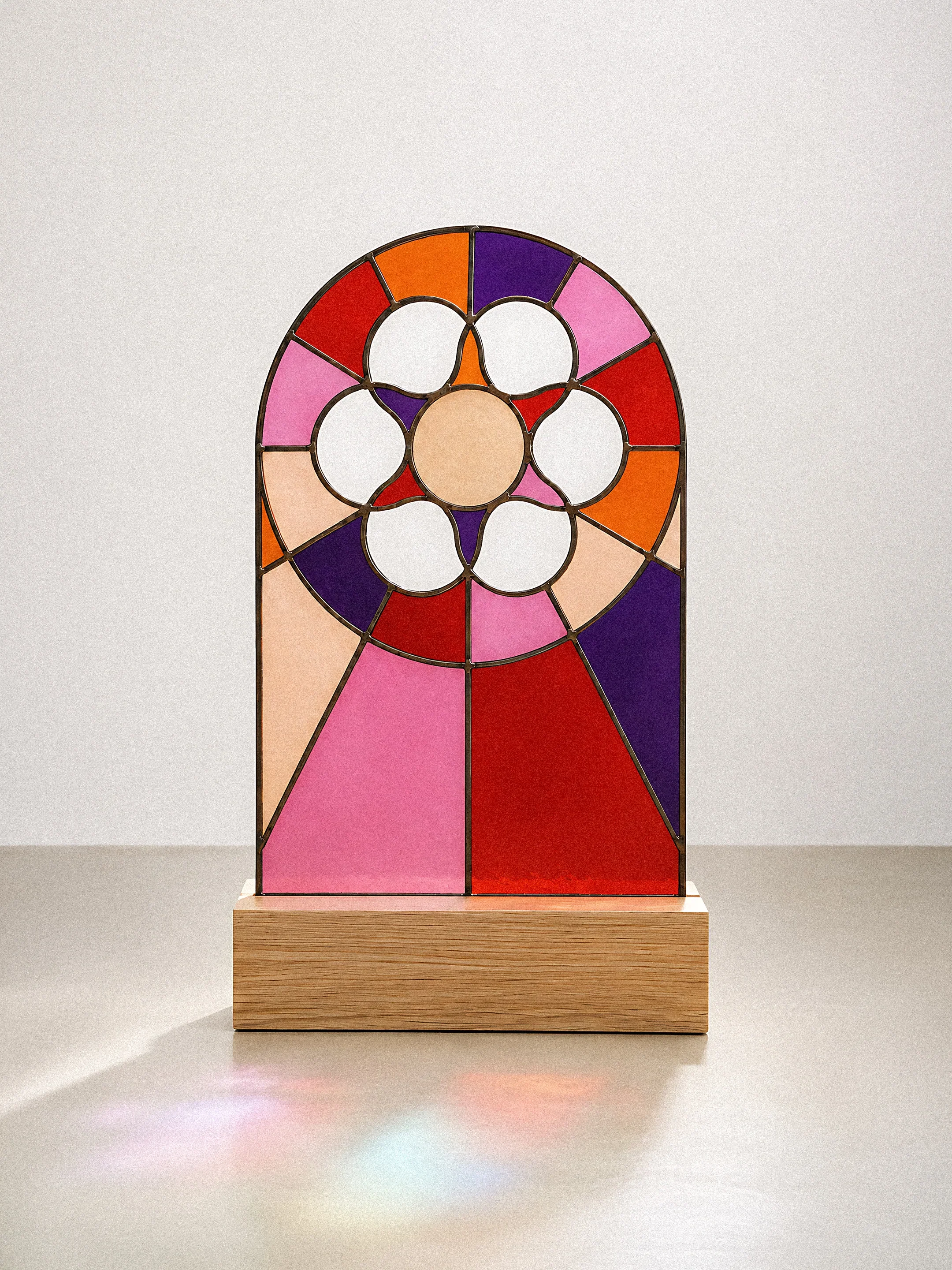 Une sculpture en verre coloré représentant un visage, posée sur une base en bois.