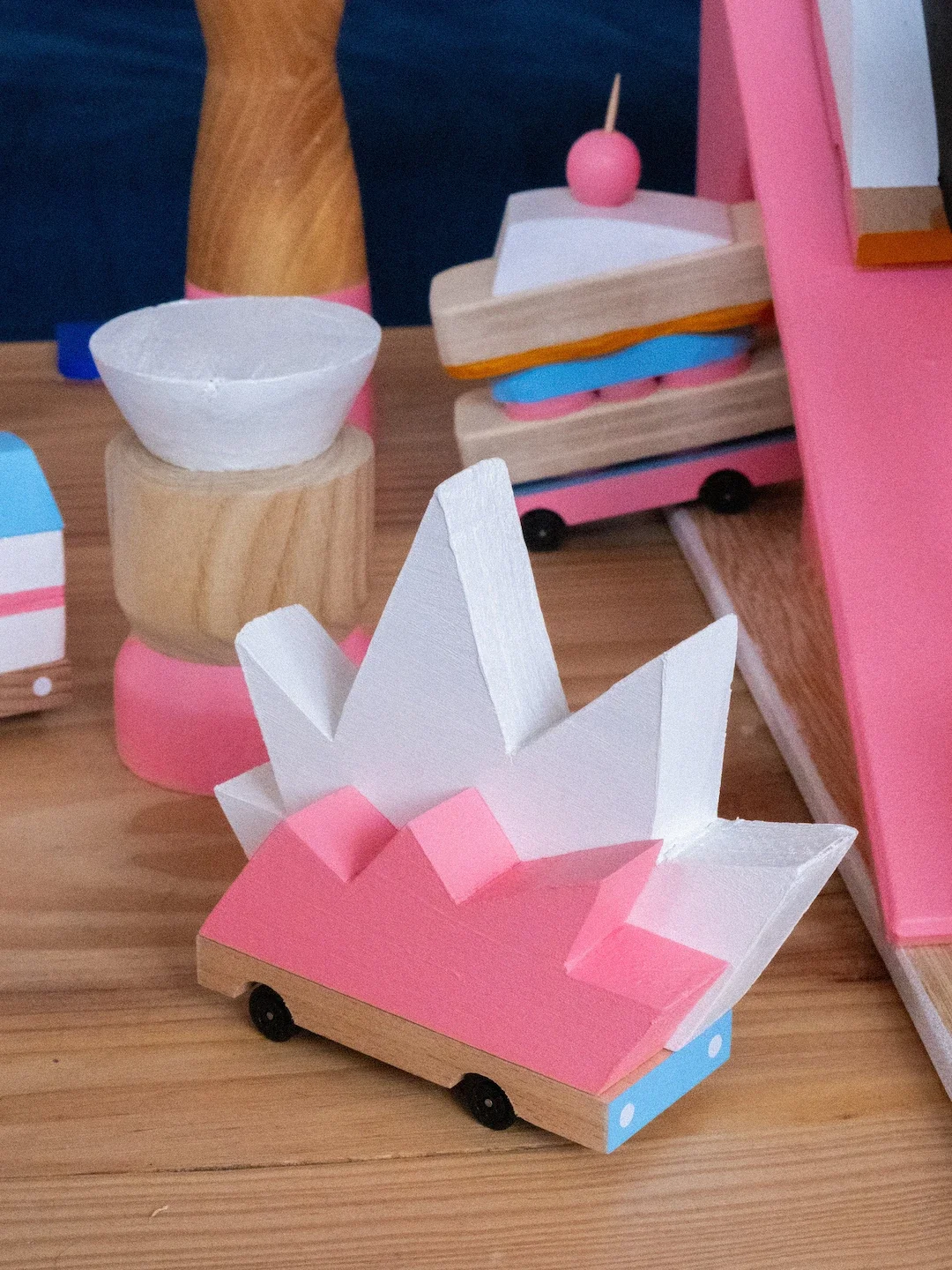 Miniature en bois peinte en rose et blanc, représentant un château ou une couronne, placé sur une surface en bois.