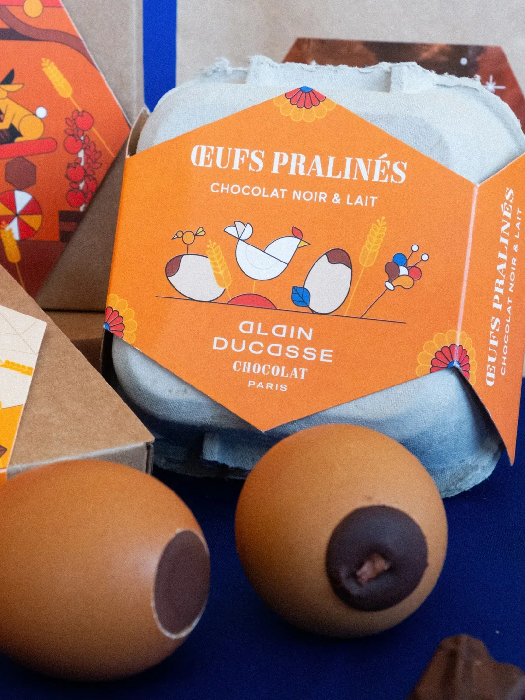 Oeufs pralinés au chocolat noir et lait, emballage coloré avec illustrations de poules, grains et fleurs, de la marque Alain Ducasse.