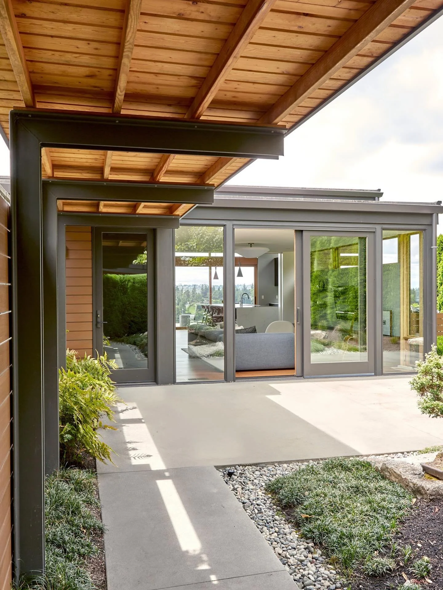 An asymmetrical steel framed canopy paired with a Pacific Ashlar dry stack stone accent wall defines the walkway of the lush courtyard garden at our #MCT_HilltopHouse connecting the detached garage to the den and great room. Visit our website linked 