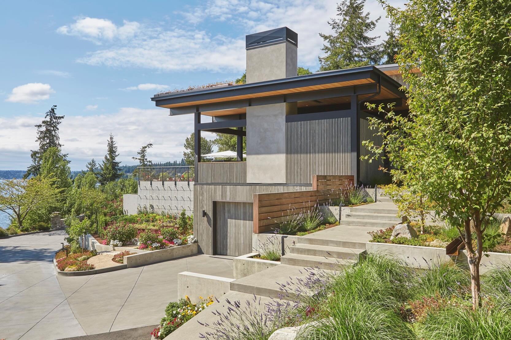 Positioned atop a hillside with panoramic views of Lake Washington, the dramatic tiered concrete path leads to an oversized steel door at our #MCT_PerchHouse. Flanked by lush landscaping equipped with a continuous free flowing water feature and woode