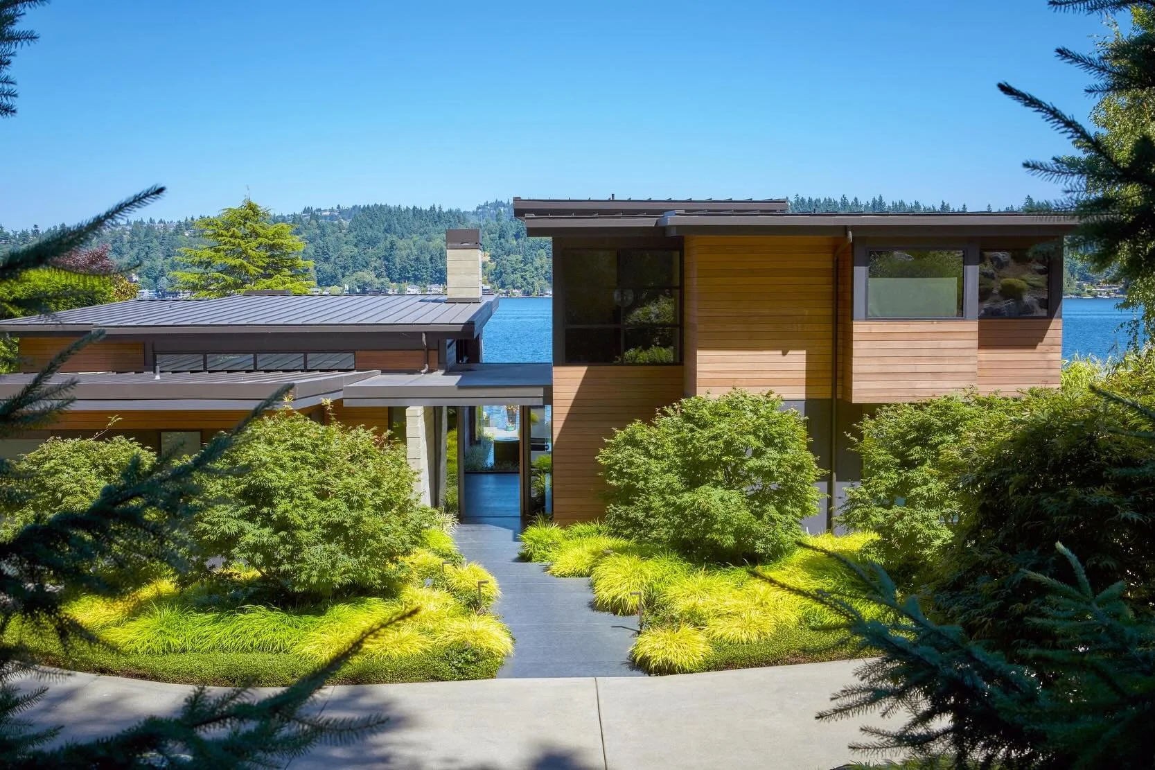 Sitting atop a sloped site along an angled shoreline, lush landscaping defines the entry at our #MCT_EastlightHouse to reveal a water feature that opens up to expansive lake views beyond. The strategic orientation of the home captures both eastern li