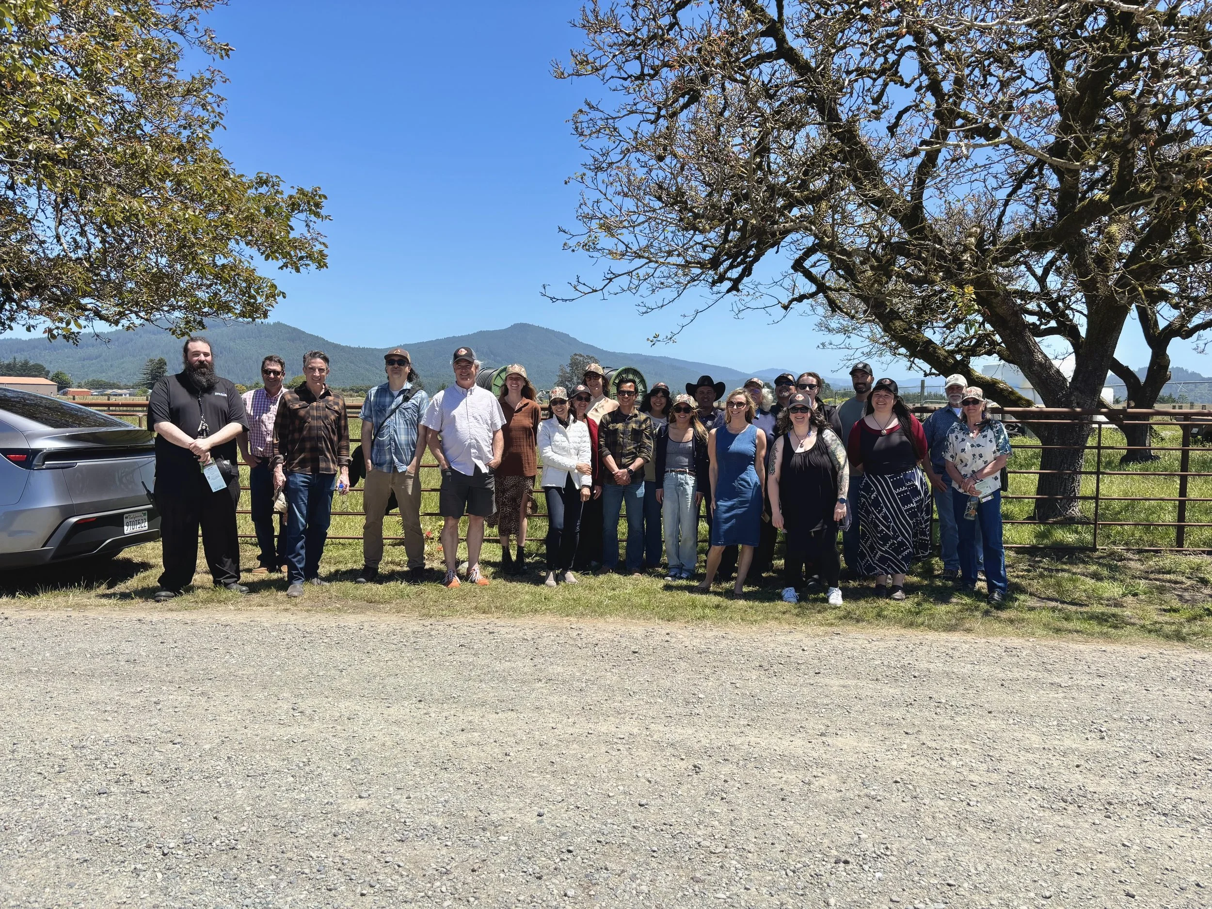 photo depicts a group of 22 people standing at the Eel River Organic Beef Ranch in front of a large tree with mountains in the background.