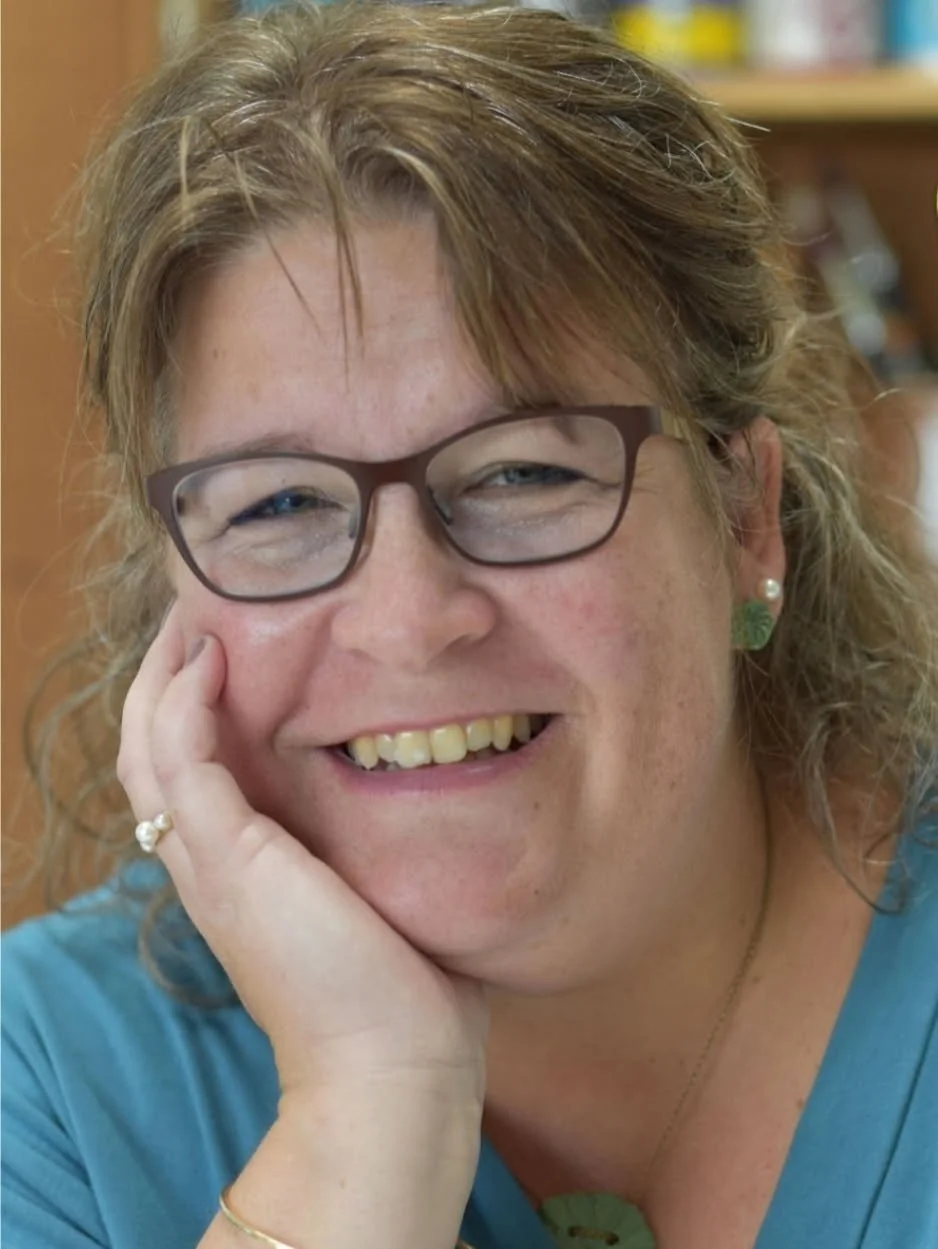 Et foto af en smilende kvinde med briller, med håret til den ene side, der hviler sit hoved på sin hånd. Danseskole i Aarhus