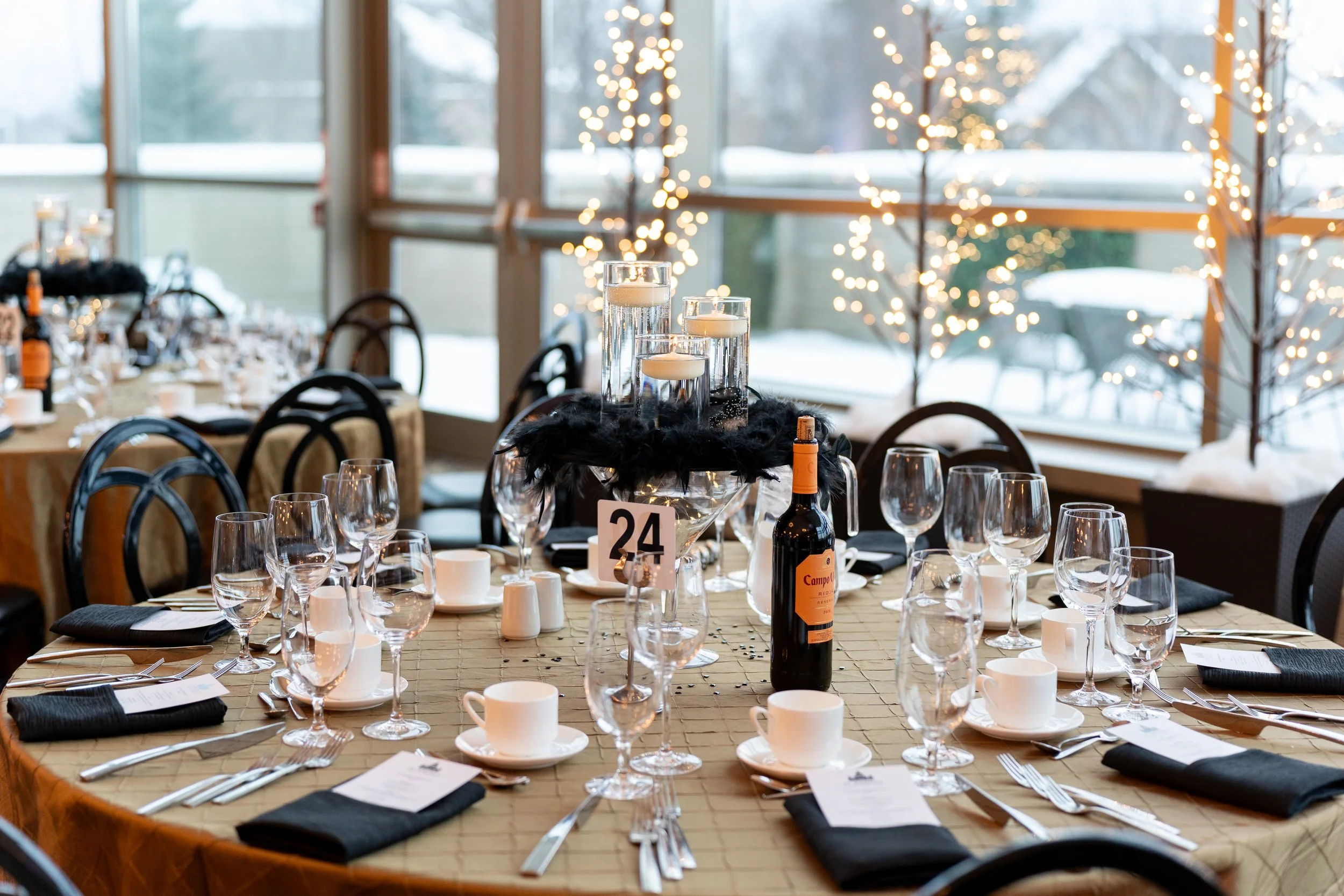 A decorated banquet table set with glasses, plates, napkins, and a bottle of wine, with candles and fairy lights in the background.