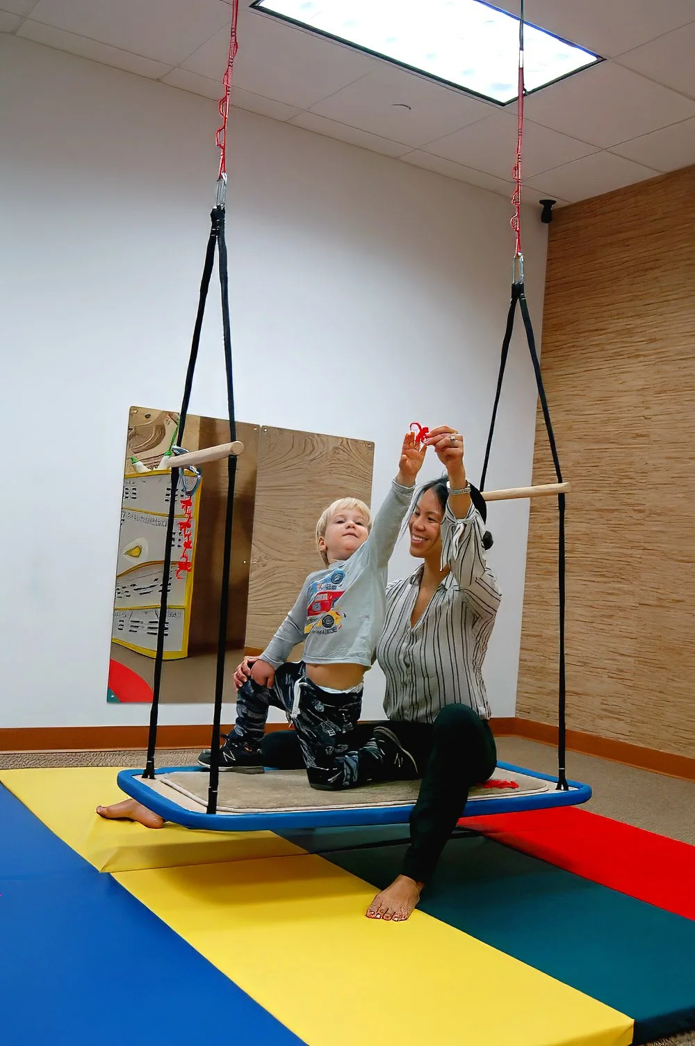 A pediatric therapist and a young child playing together on a platform swing during a therapy session