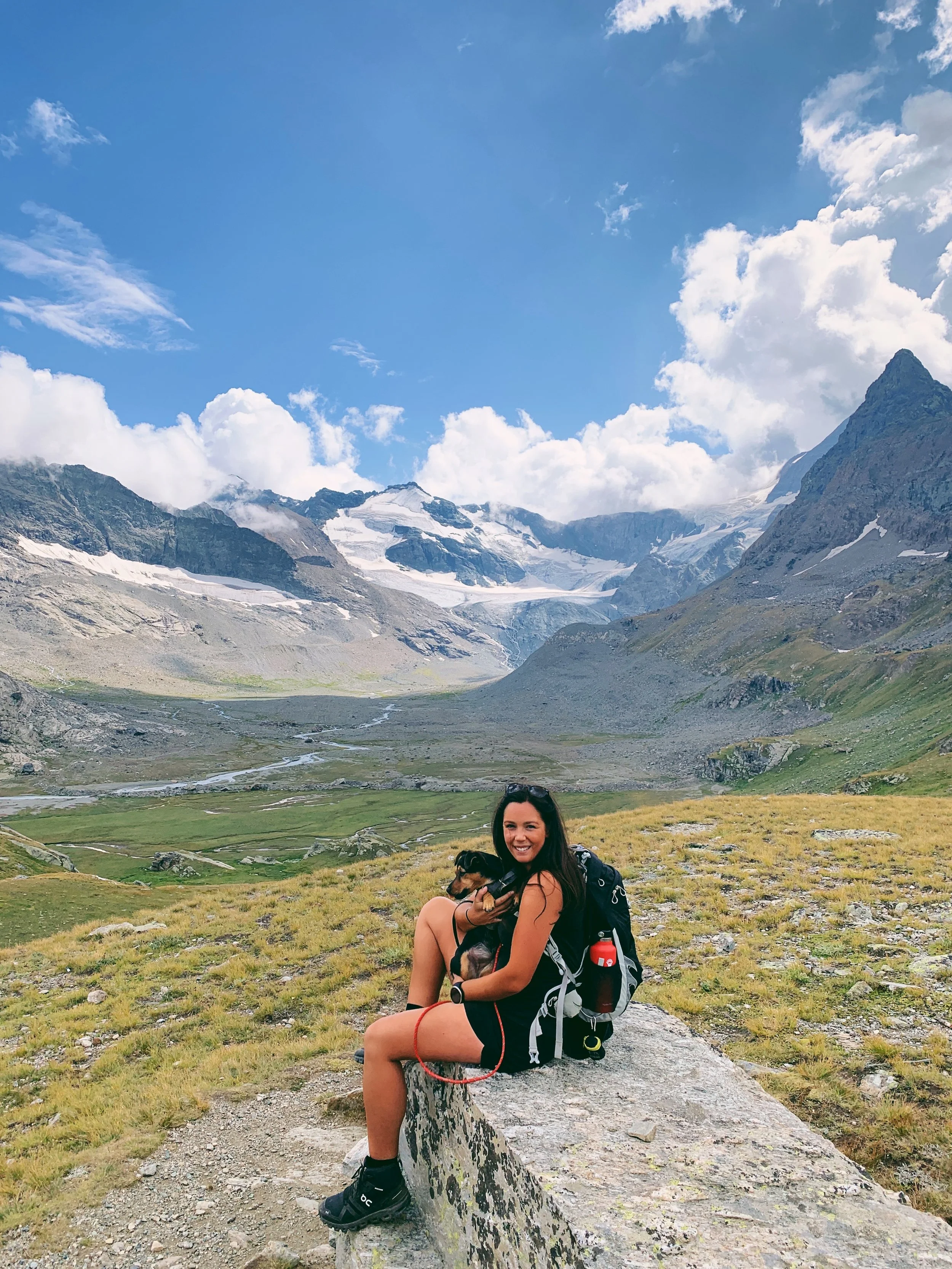Woman and dog sit on a rock at Cirque des Evettes, Savoie France