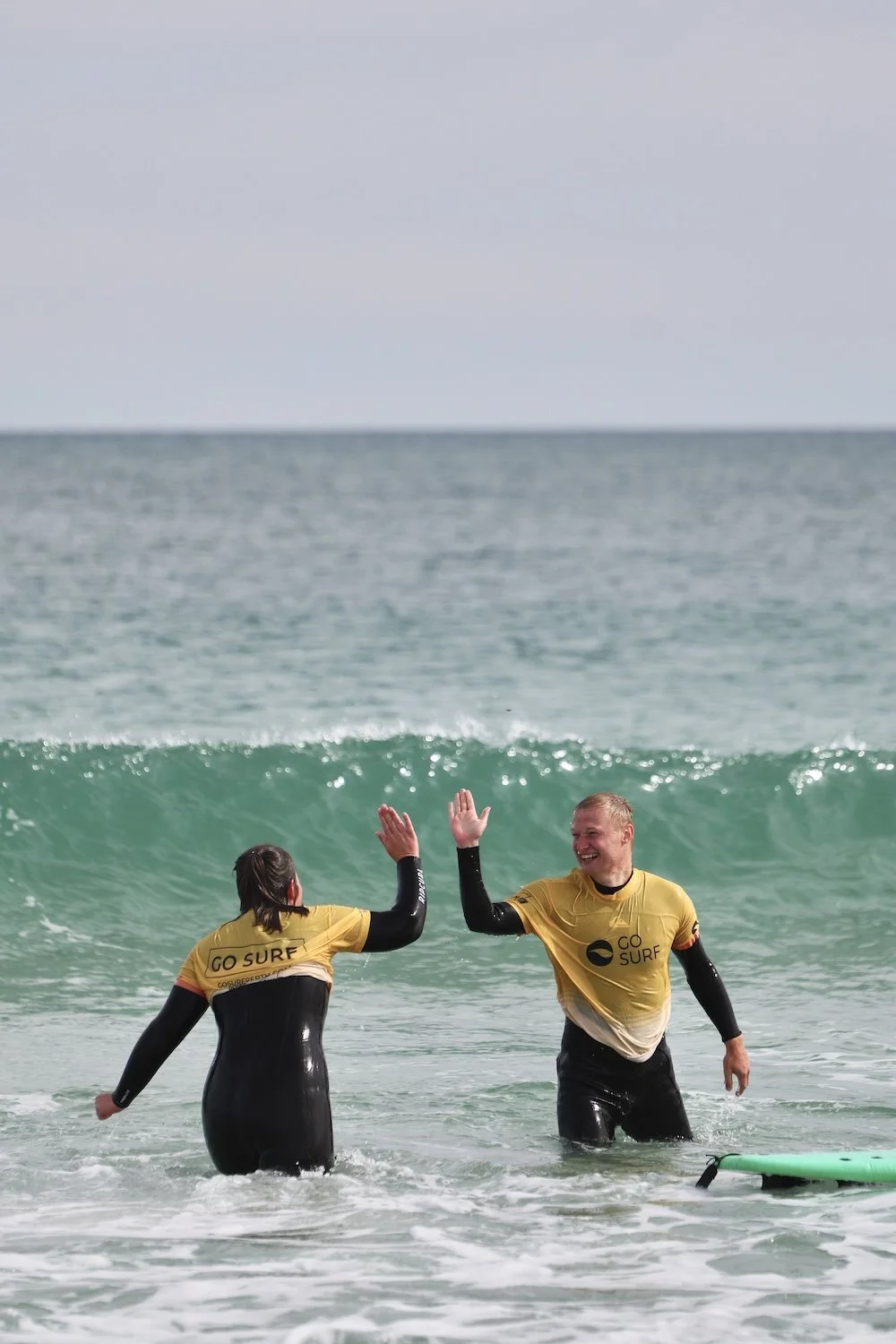 Two men in wetsuits celebrate by high-fiving each other on a beach, showcasing camaraderie and excitement.