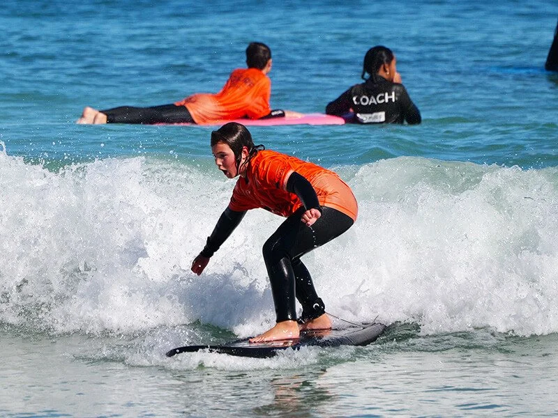 * Child catching first wave during beginner surf lesson at Leighton Beach