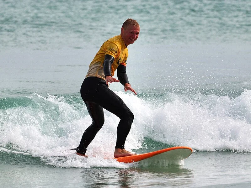 A man in a yellow shirt balances on a surfboard while riding a wave in the ocean.