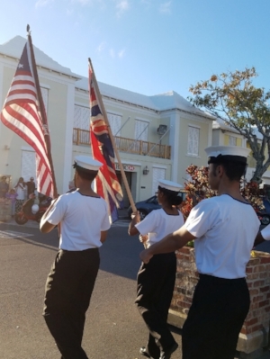 The T.S. Admiral Somers Sea Cadets of Bermuda lead the procession from the town square to St. Peter's Church in St. George's Parish, Bermuda, where the wreath-laying ceremony takes place. They carry the flag of Bermuda and the flag of the U.S. with 13 stars.